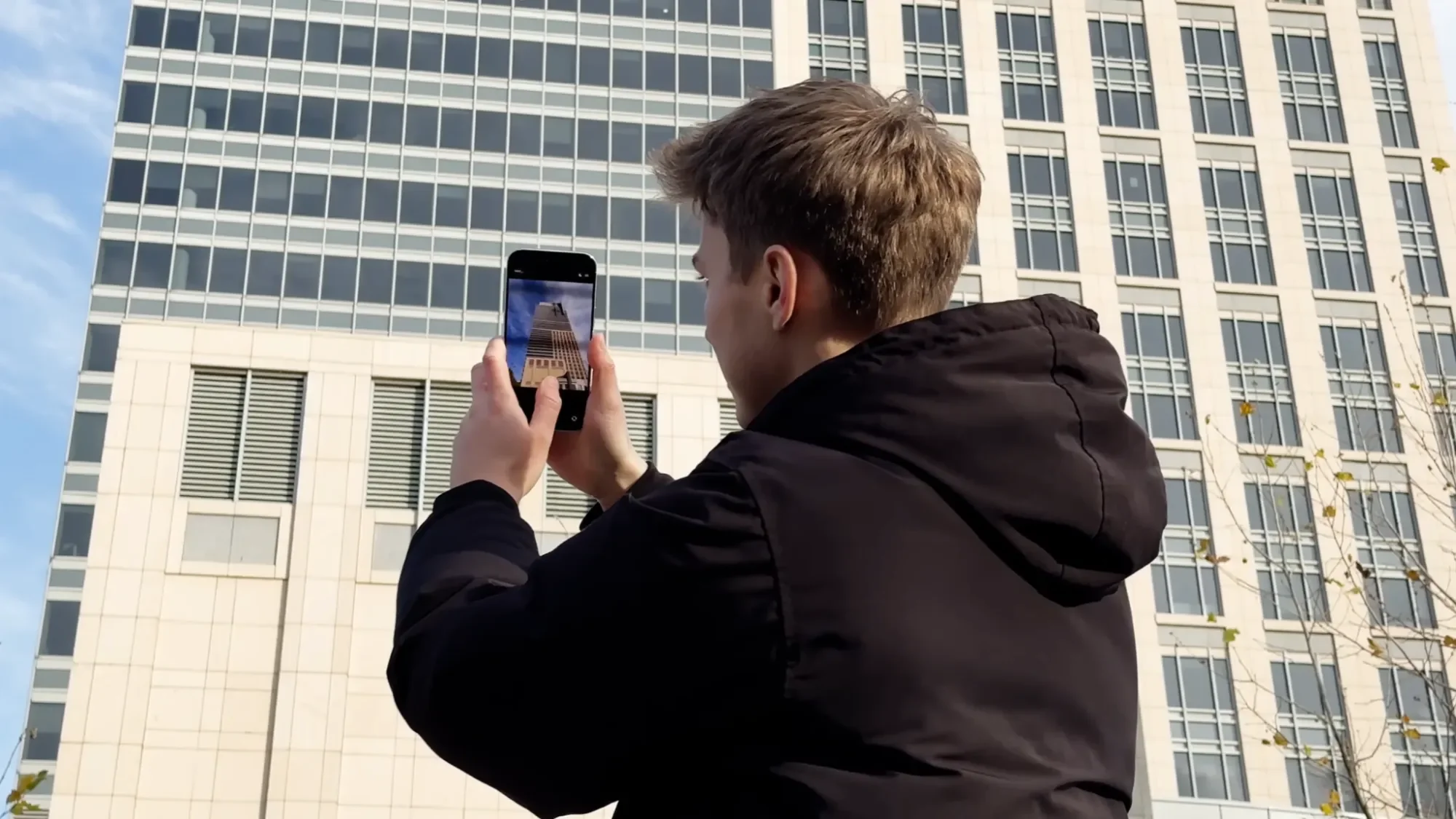 Man taking a photo with an iPhone Air in front of an office building