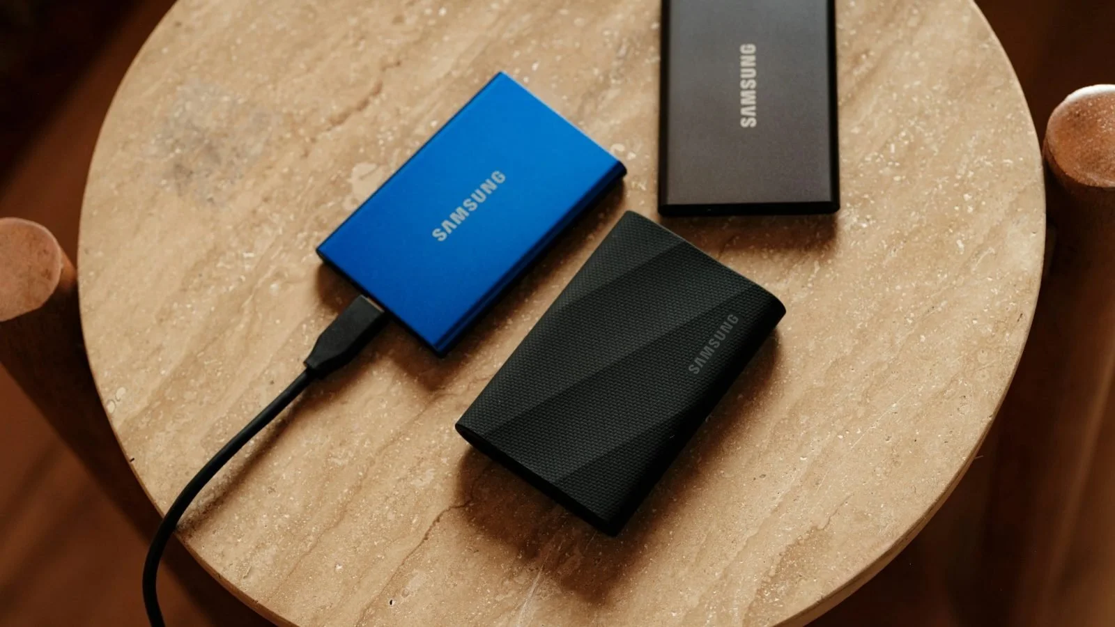 Three portable SSDs with a USB-C cable on a wooden table