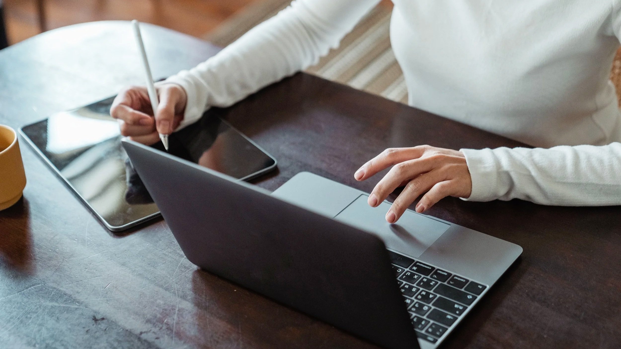 A woman using a tablet and a laptop simultaneously