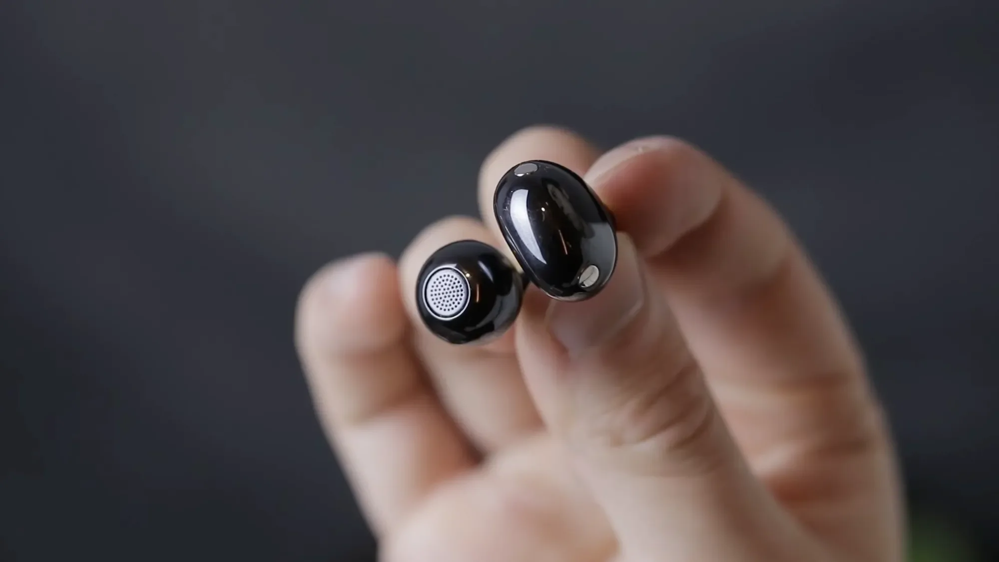 Hand holding a black Huawei FreeClip 2 earbud