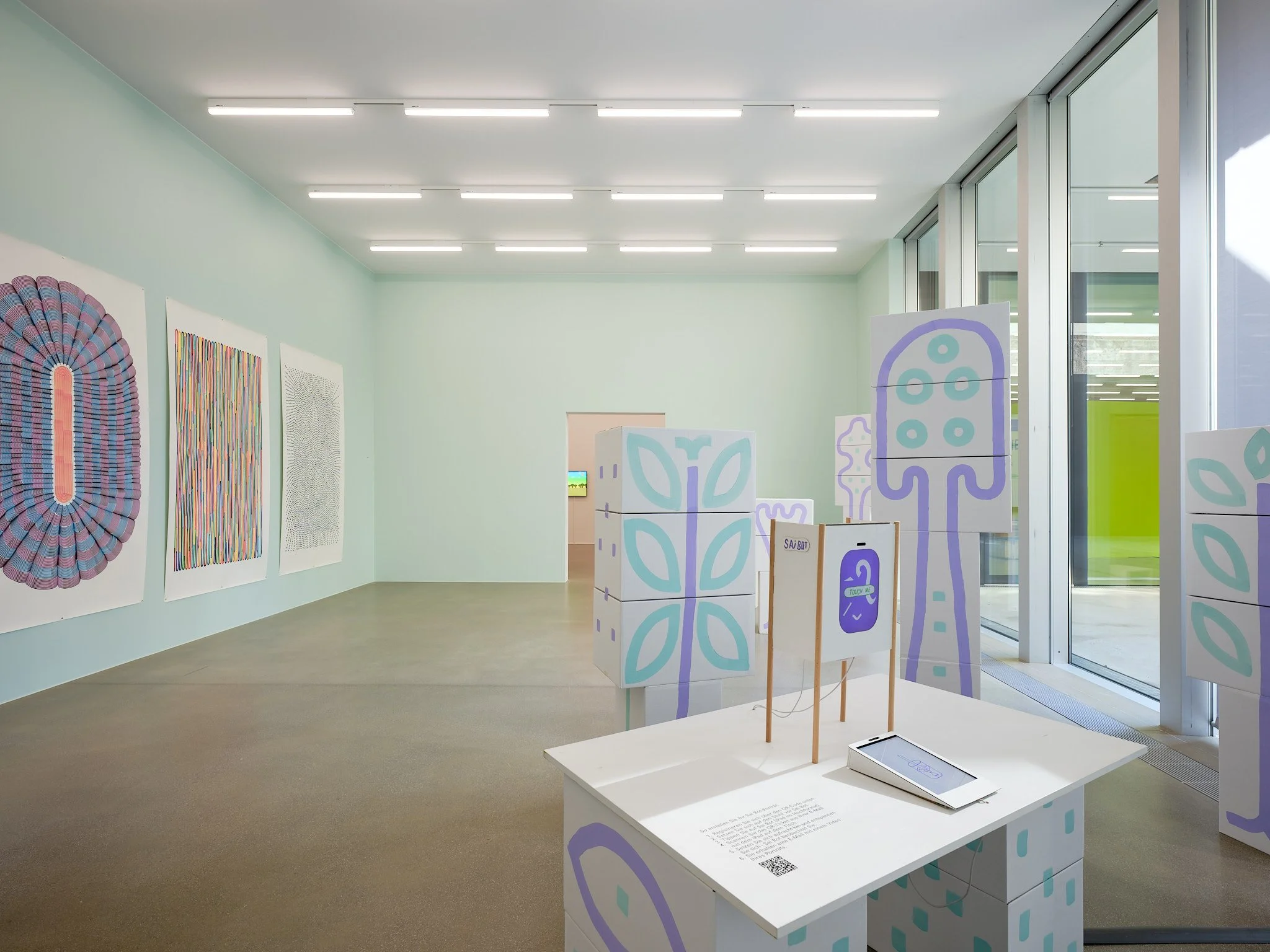 Exhibition room at Aargauer Kunsthaus with the Sai Bot station, painted cardboard figures and a window front