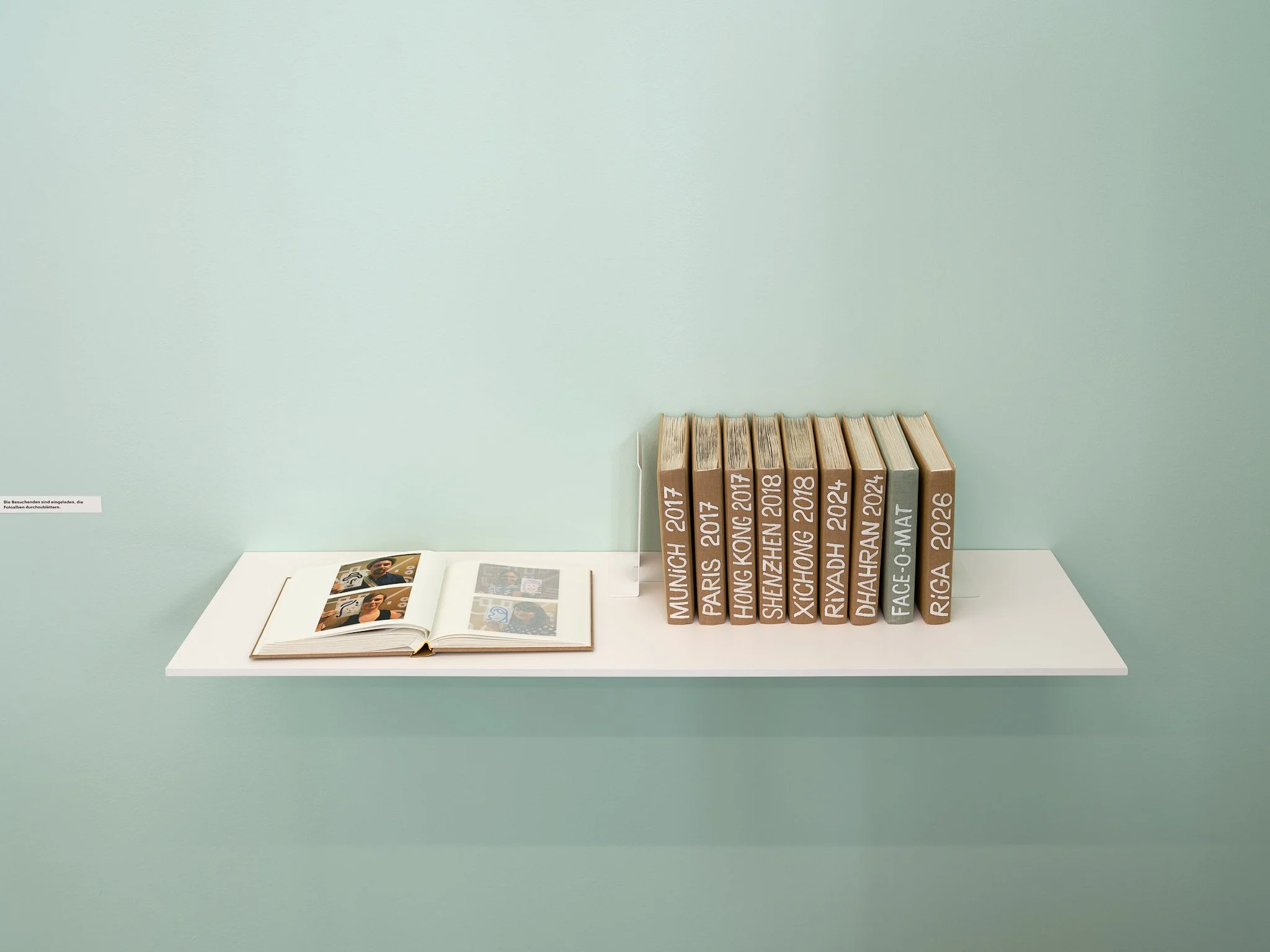 Shelf with Face-o-mat photo albums labelled by city and year, from Munich 2017 to Riga 2026, one album open