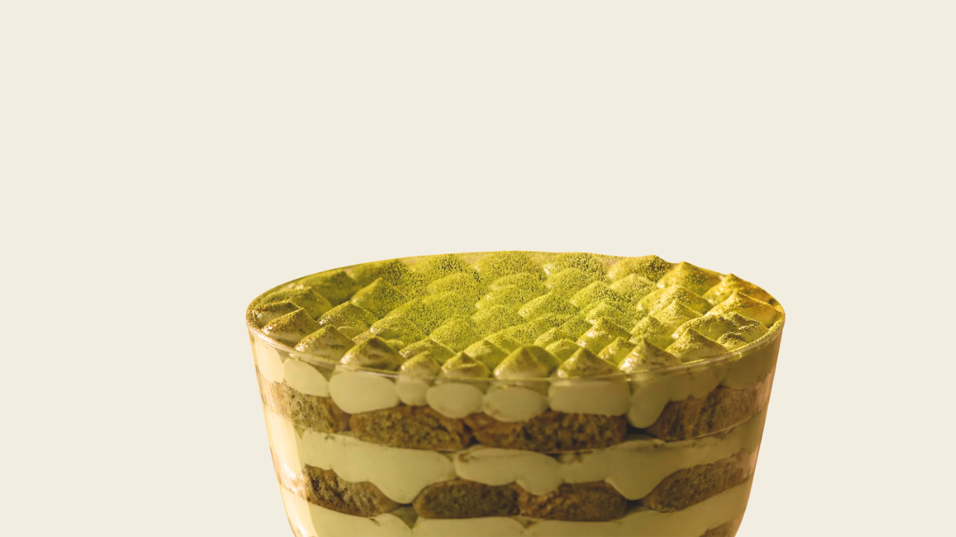 Close-up of a layered matcha tiramisu dessert in a glass cup with layers of biscuit and cream.