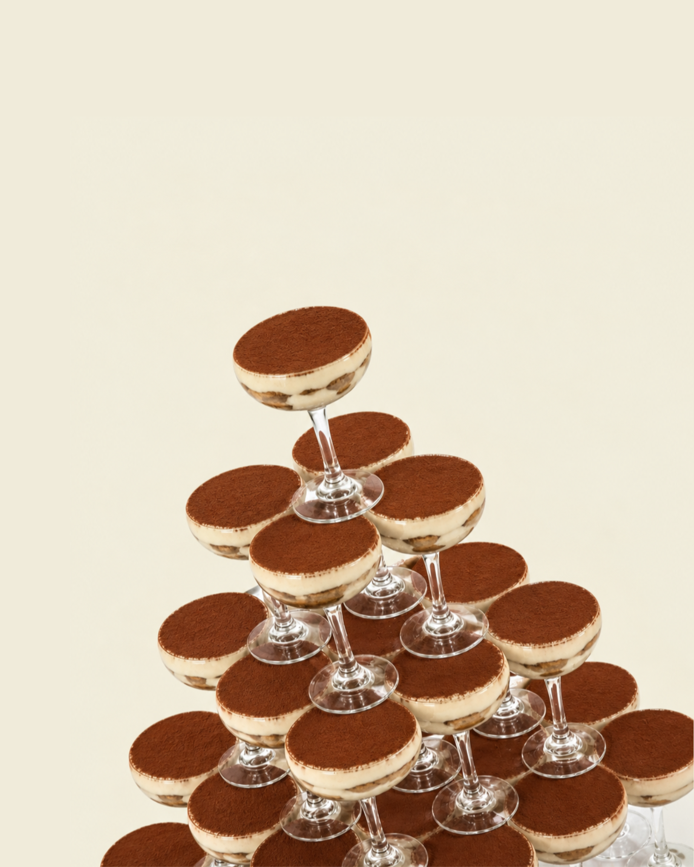 Tiered pyramid of glass dessert cups filled with tiramisu, topped with cocoa powder, against a light beige background.