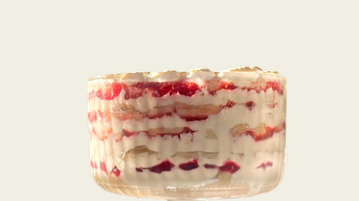 Close-up of a layered strawberry parfait in a clear glass cup with whipped cream topping.