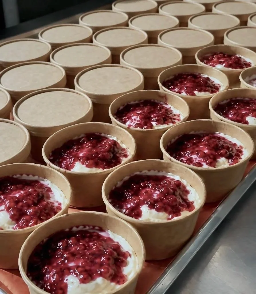 Many small bowls of dessert with a red berry topping and a cream base arranged on a tray.