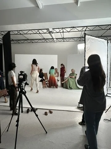 People preparing for a photo shoot in a studio with a white backdrop, camera equipment, and lighting