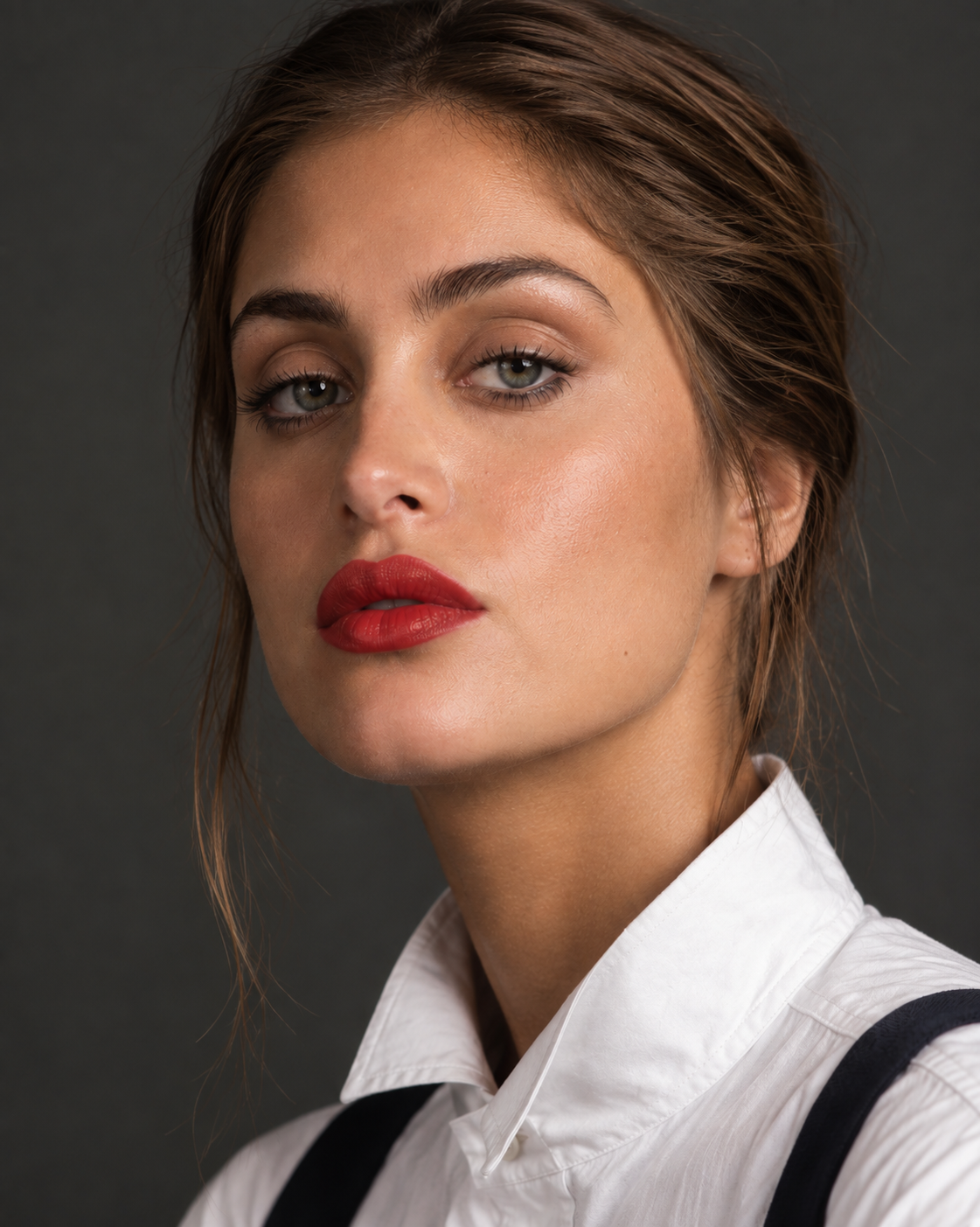 Portrait of a woman with light skin, brown hair, and blue eyes wearing red lipstick, a white shirt, and black suspenders.