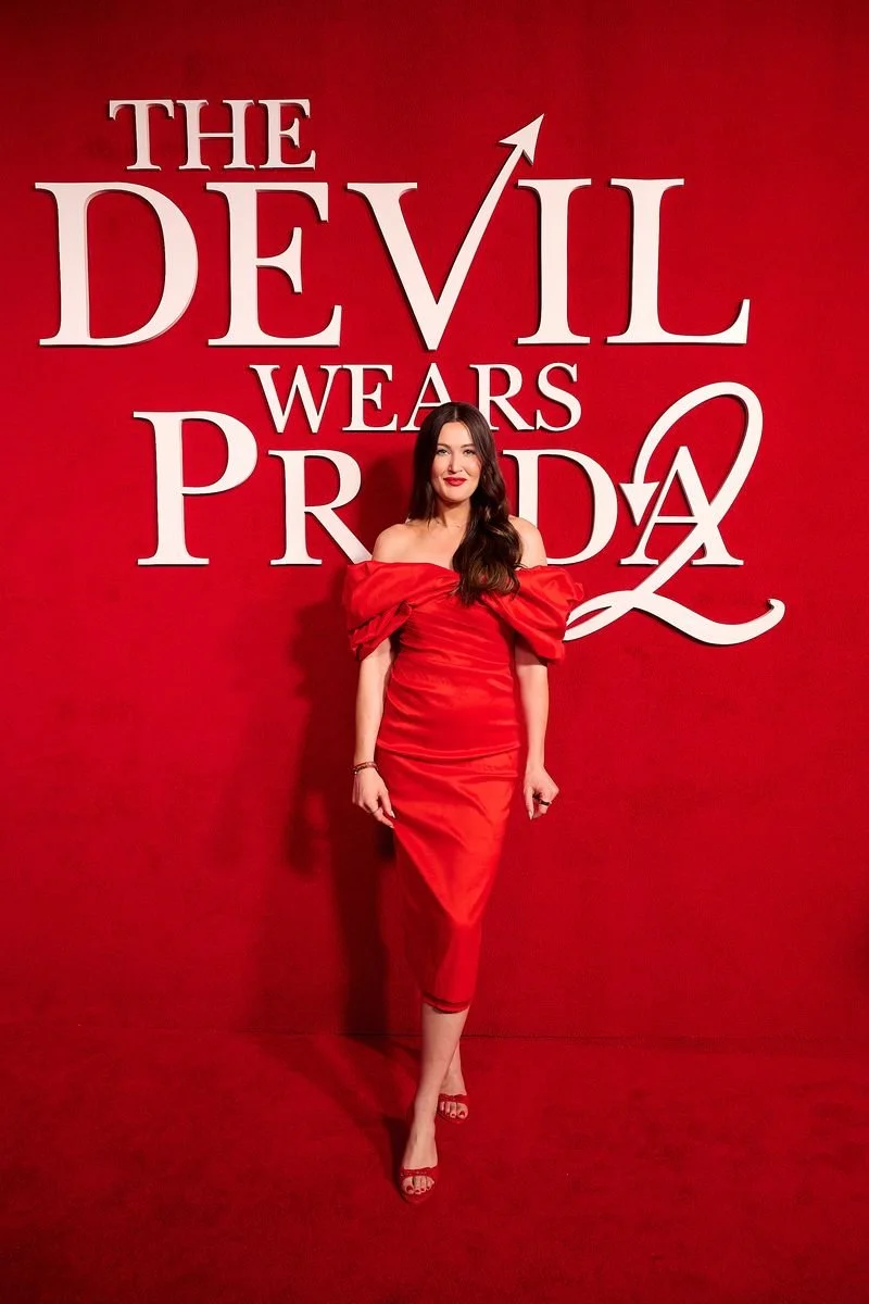 A woman in a red dress and red heels standing in front of a red background with large white text that reads 'The Devil Wears Prada'.
