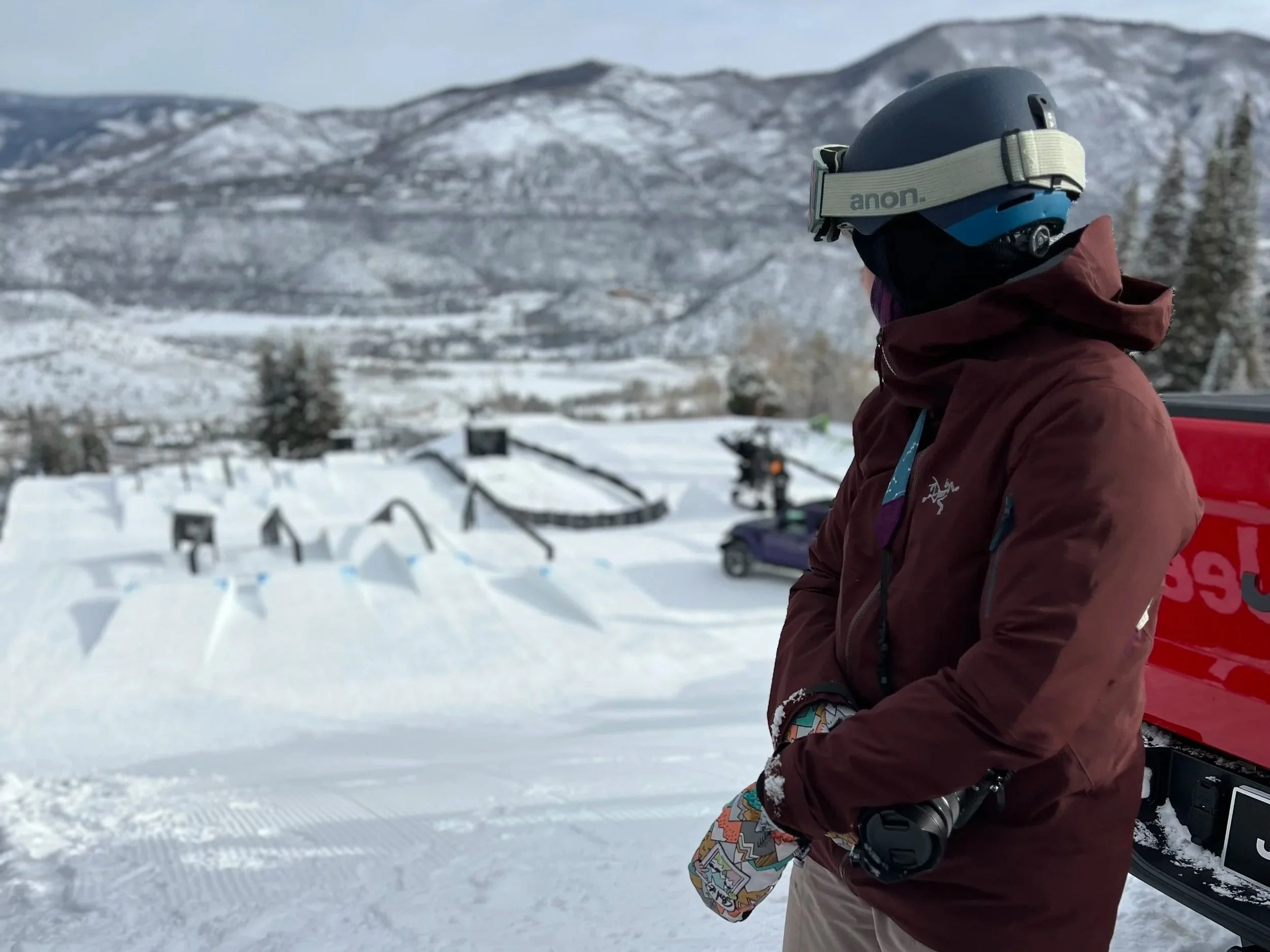 A person wearing a helmet and winter gear standing in a snowy landscape with mountains in the background.