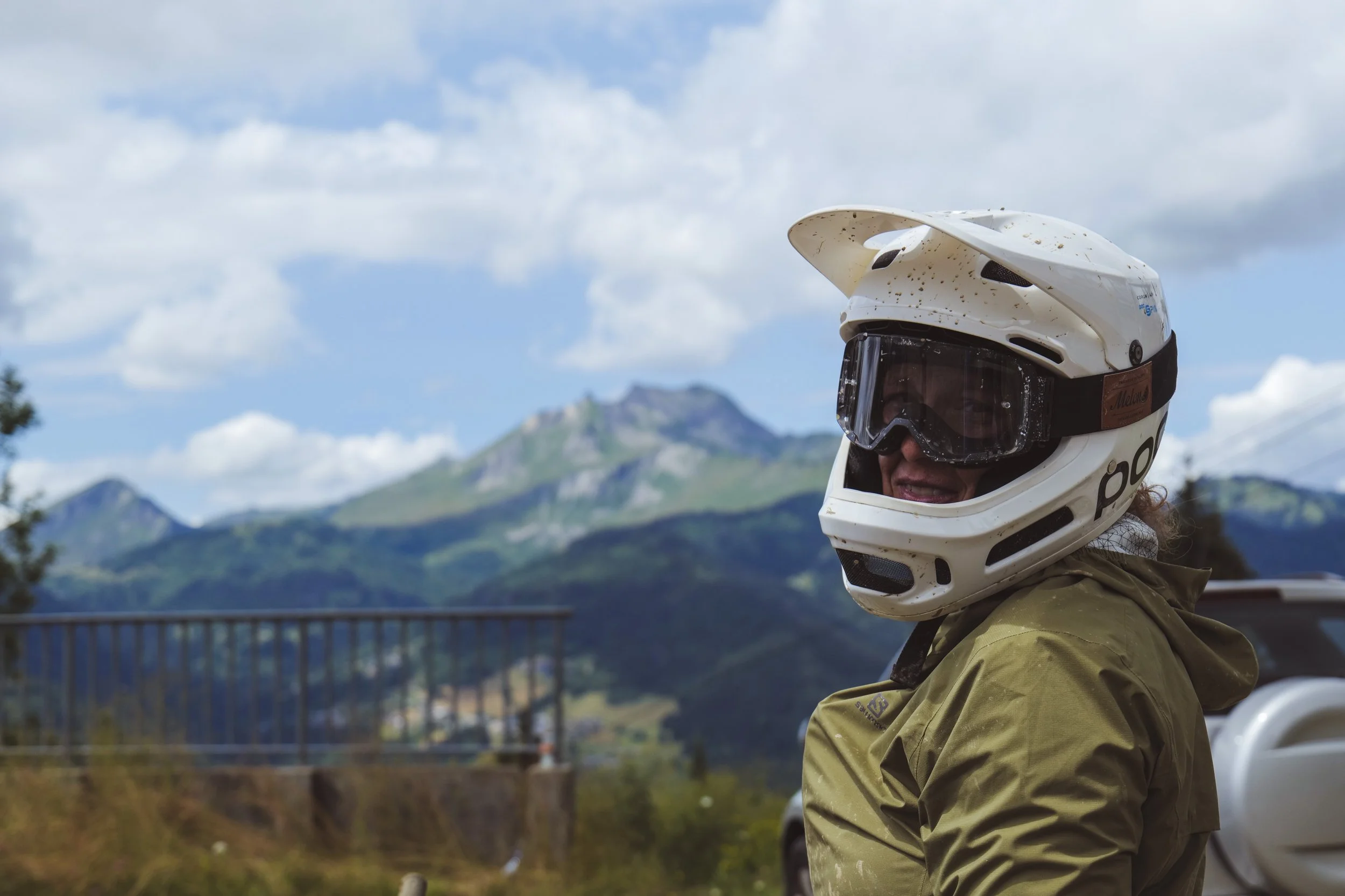 Person wearing a helmet with goggles, outdoors with mountains and a partly cloudy sky in the background.