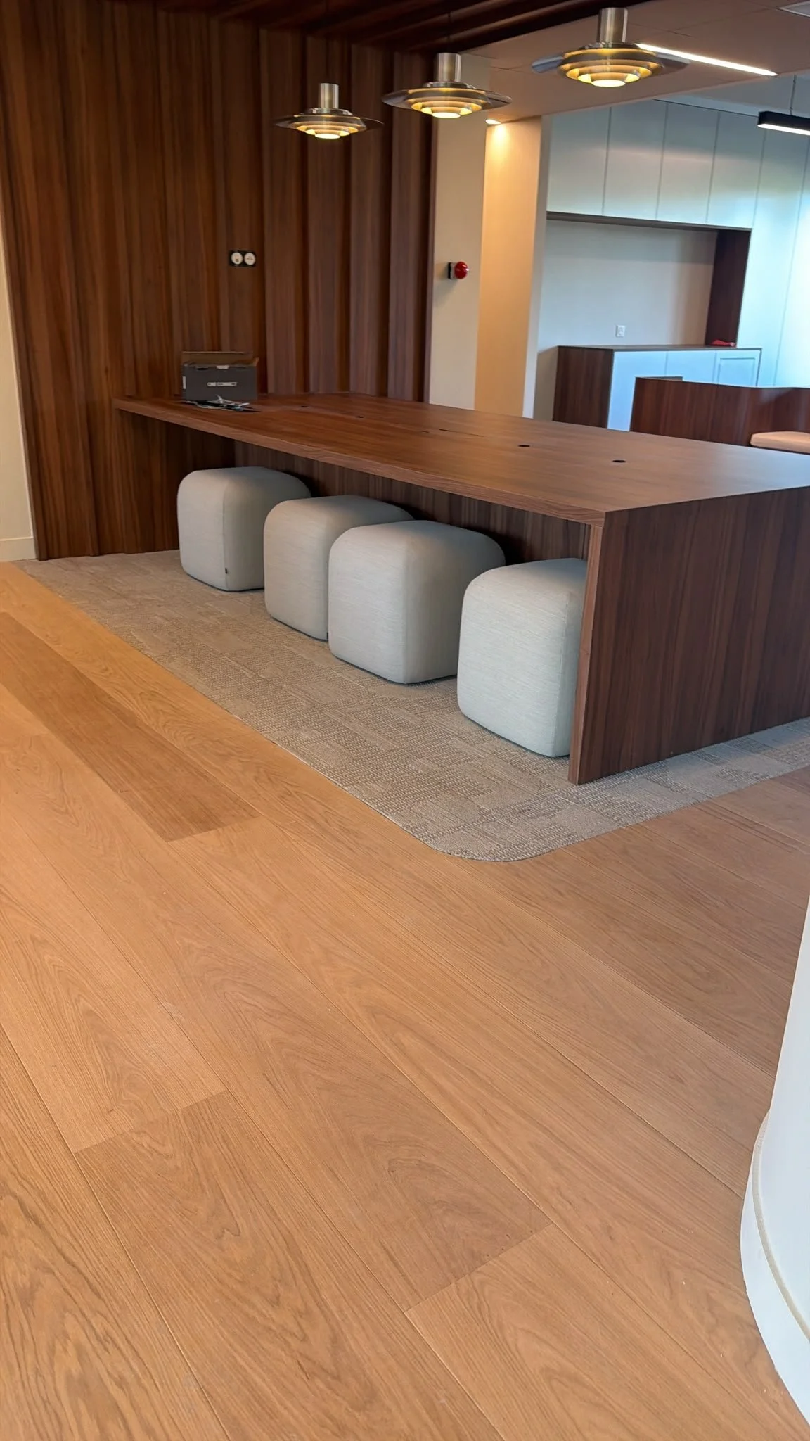 Espace de réception moderne avec comptoir en bois, quatre poufs gris et suspensions décoratives.