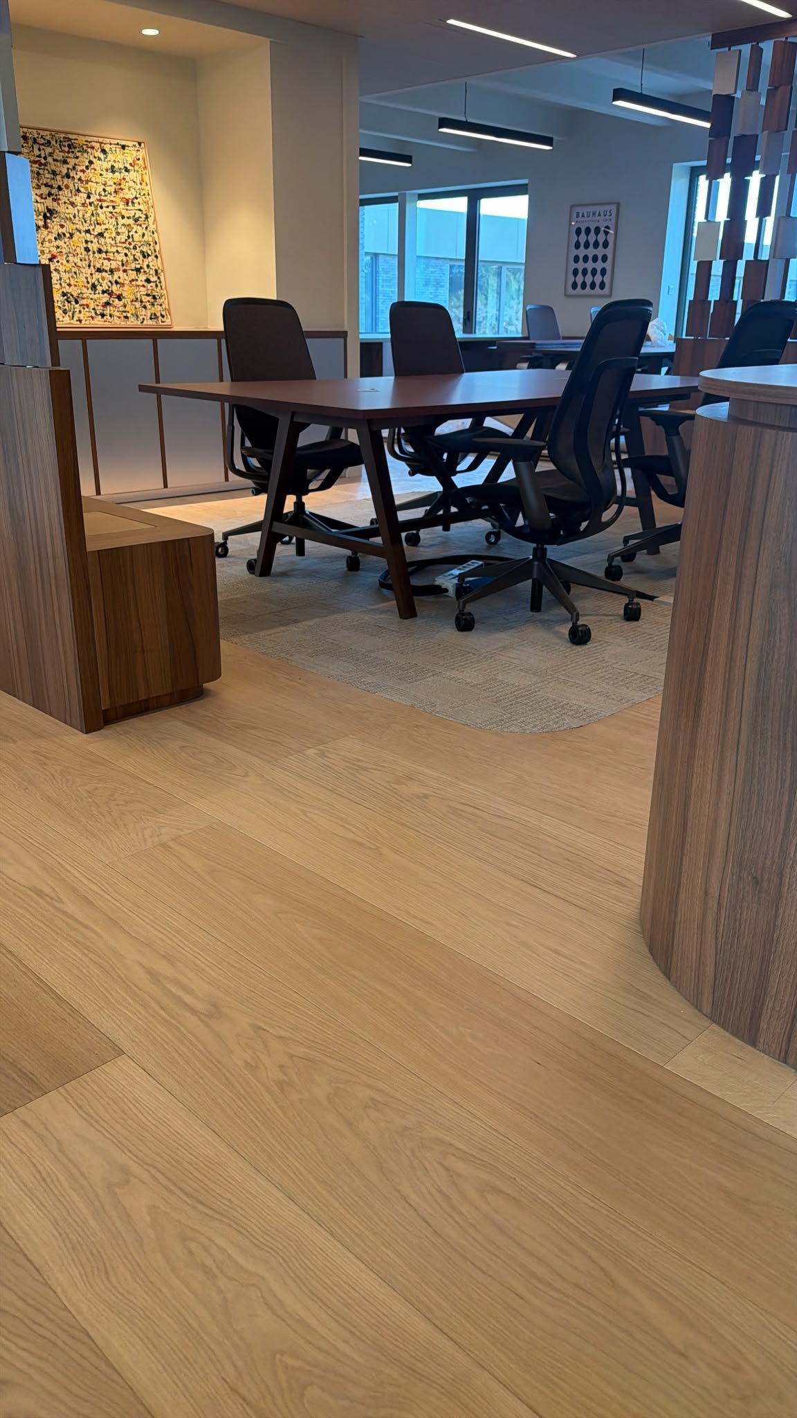 Salle de réunion moderne avec table en bois, chaises de bureau noires, parquet clair et affiches artistiques.