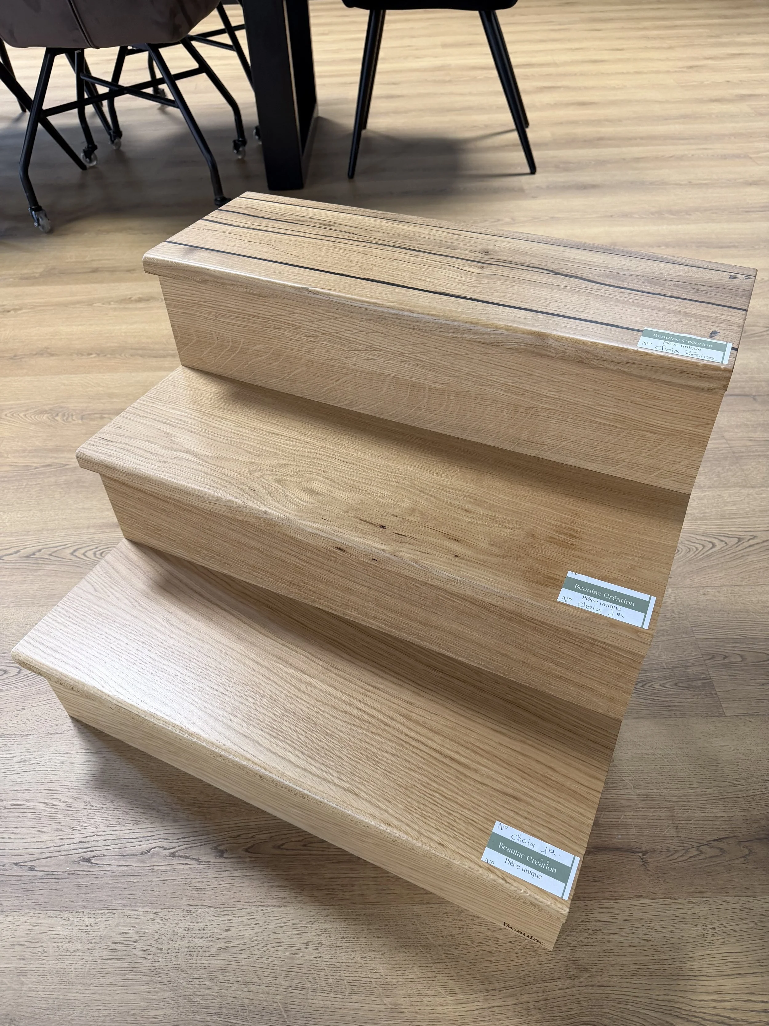 Escalier contemporain en bois clair exposé dans un showroom, avec échantillons, chaises et table en arrière-plan.