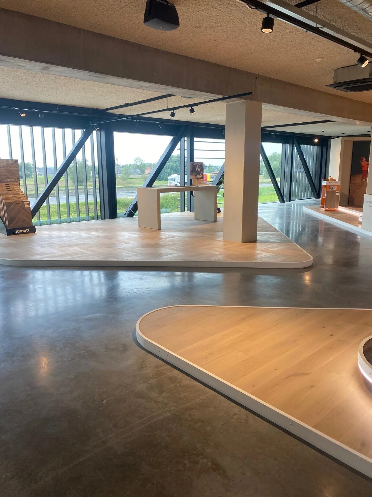 Intérieur moderne d’un espace d’exposition avec vitrines, éclairage sur rails et grandes baies vitrées donnant sur un paysage verdoyant.