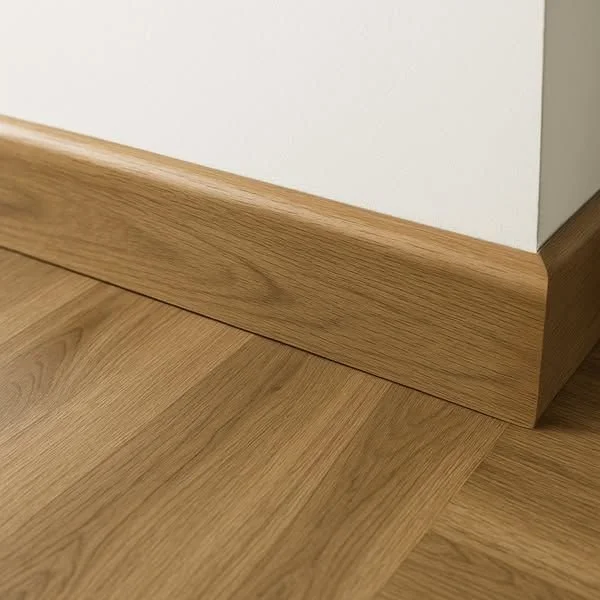 Plinthe en bois clair assortie à un parquet stratifié, dans l’angle d’un mur blanc.