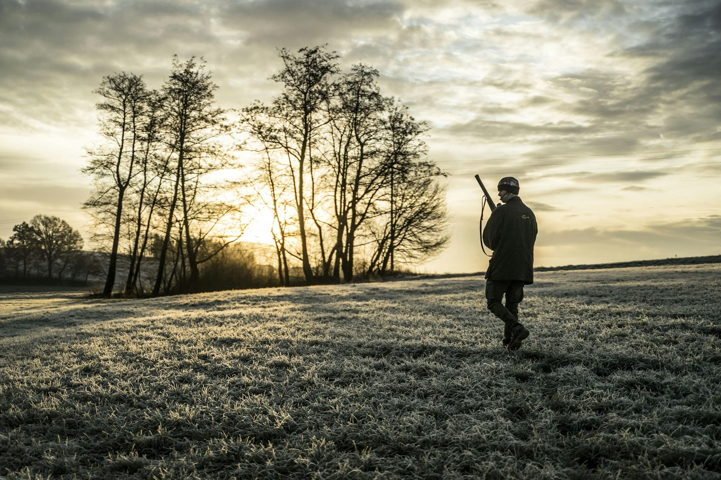 Jäger läuft bei Sonnenuntergang durch eine winterliche Landschaft mit kahlen Bäumen.