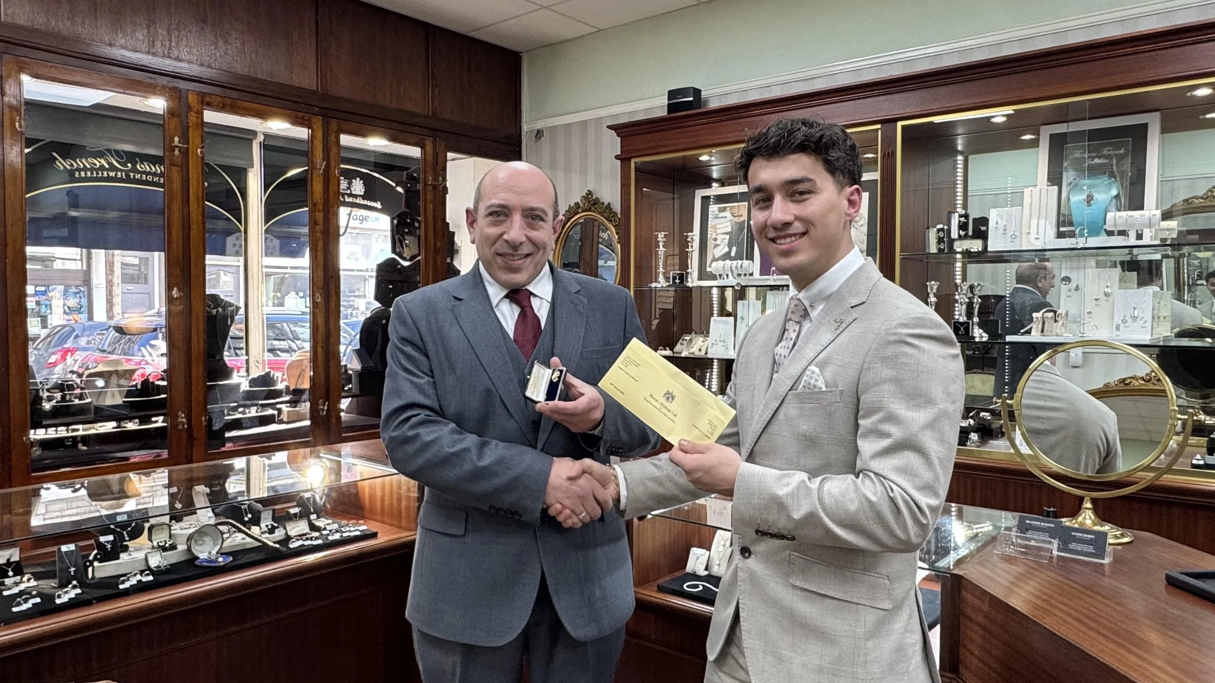 Conor Mason from Mason Jewellers and Mason Fine Acquisitons and Matt Mizzi from shaking hands inside Thomas French Jewellers in Bexhill, Conor is awarding Matt his 9ct gold Mermaid pin to signify 1 year of service at Mason Jewellers group