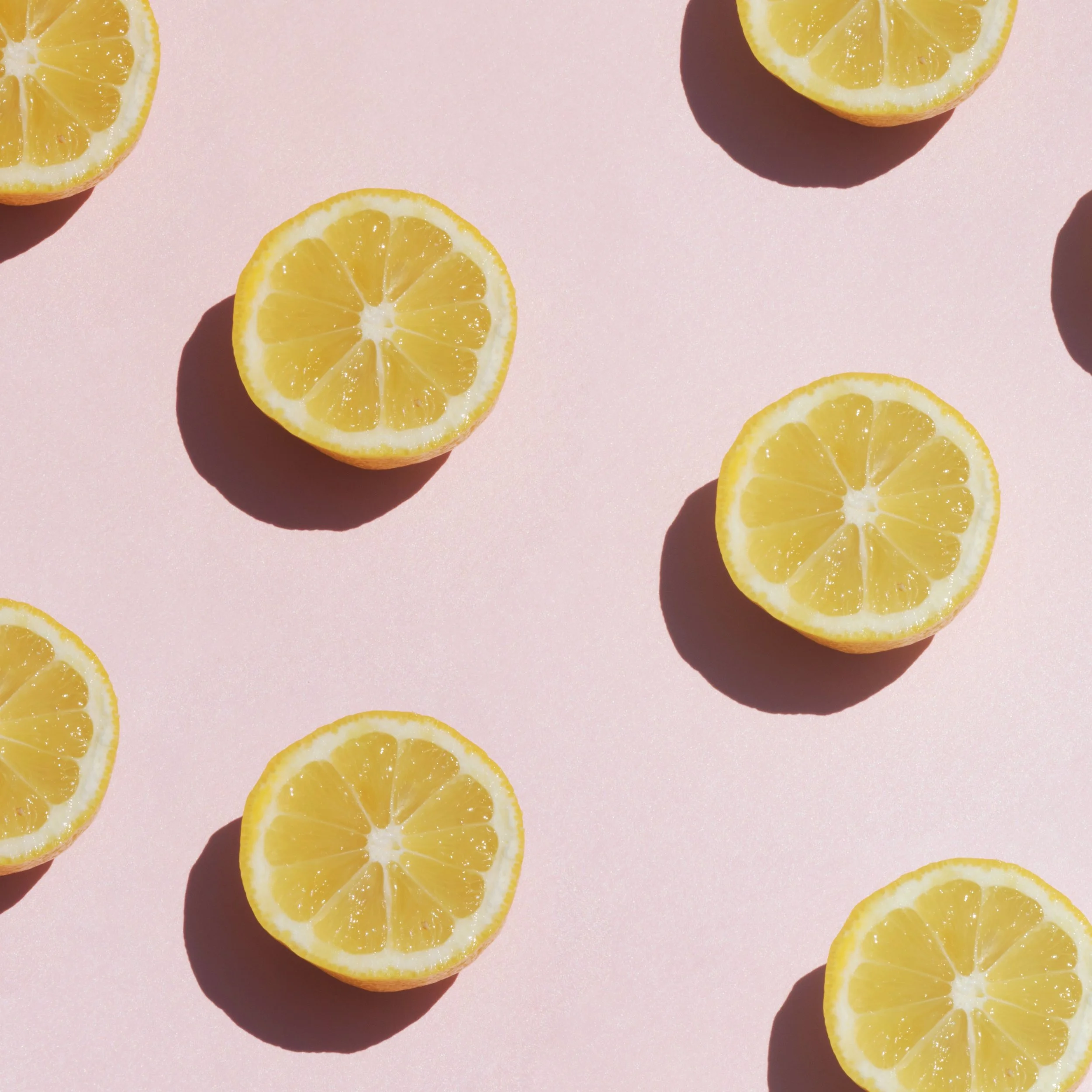 Slices of lemon scattered on a pink surface with shadows.