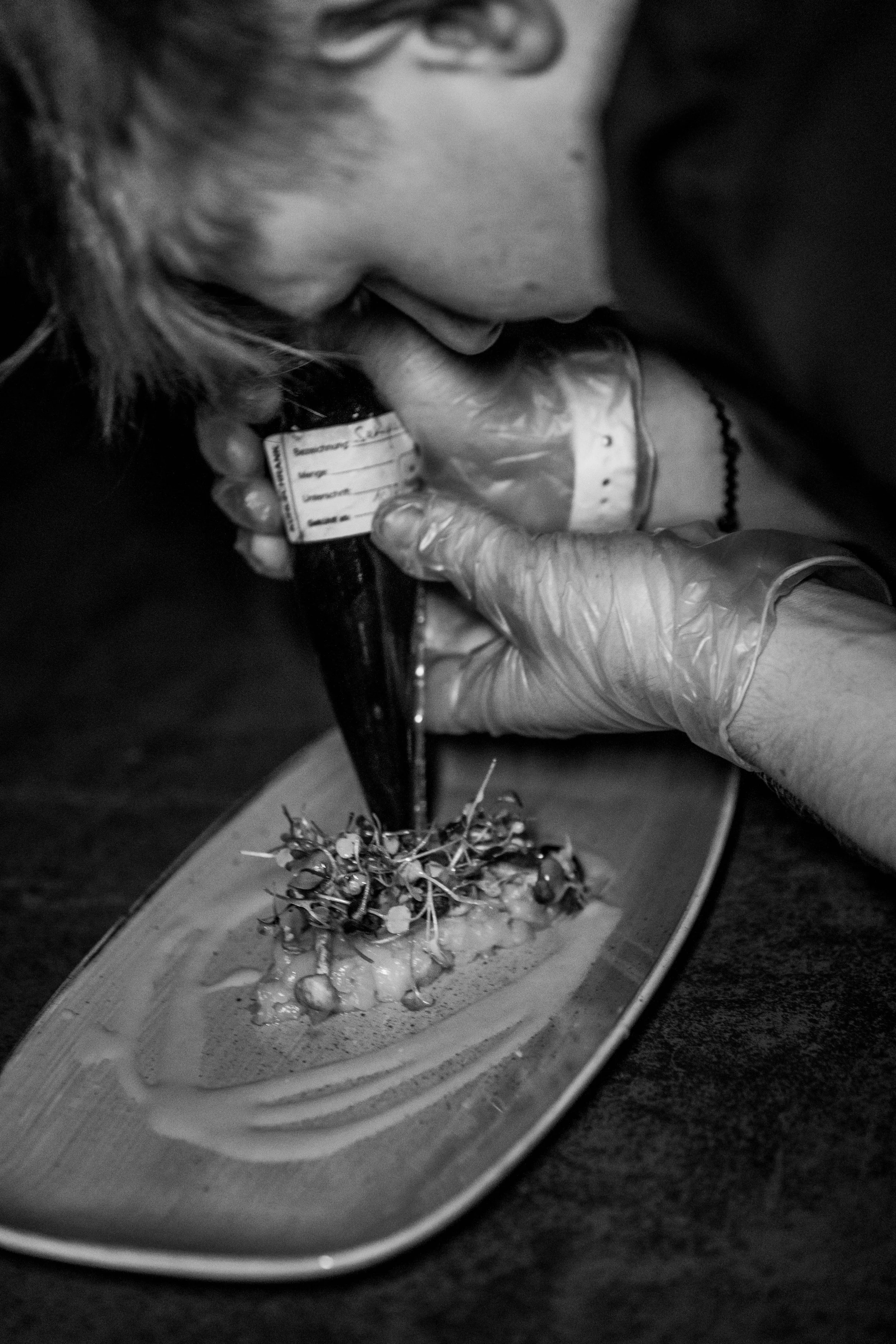 Server leaning over a plate with food, microgreens, or herbs, applyig sauce