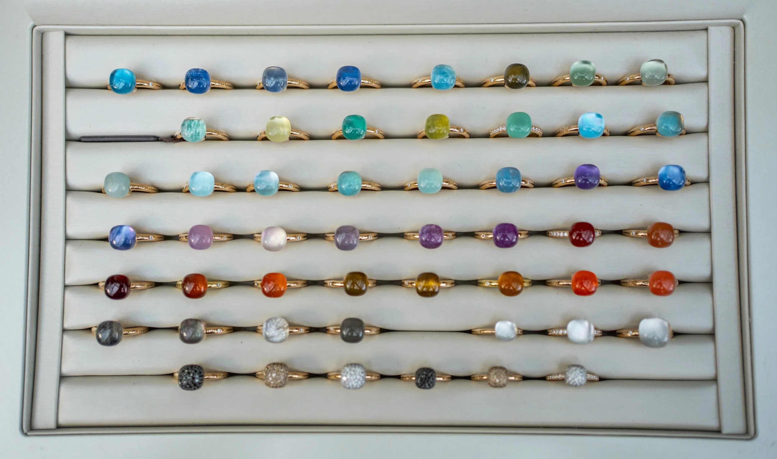A display case with multiple rows of color-coded rings featuring large, irregularly shaped gemstones in various hues.