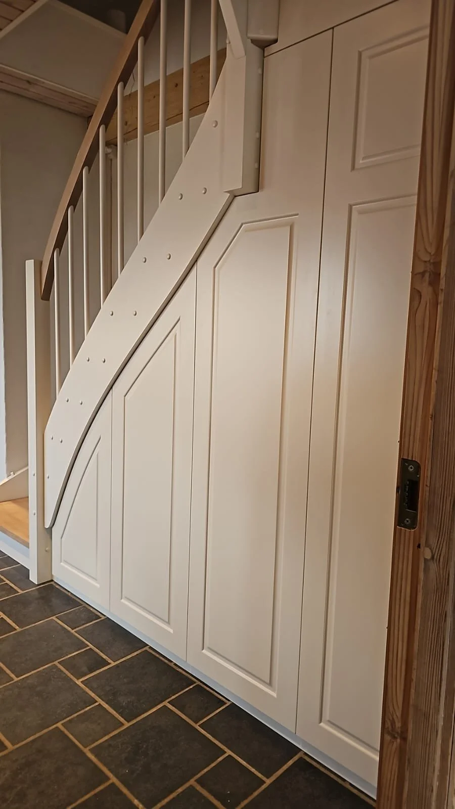 White built-in cabinet with a folding door, next to a wooden staircase railing and new wooden flooring tiles.