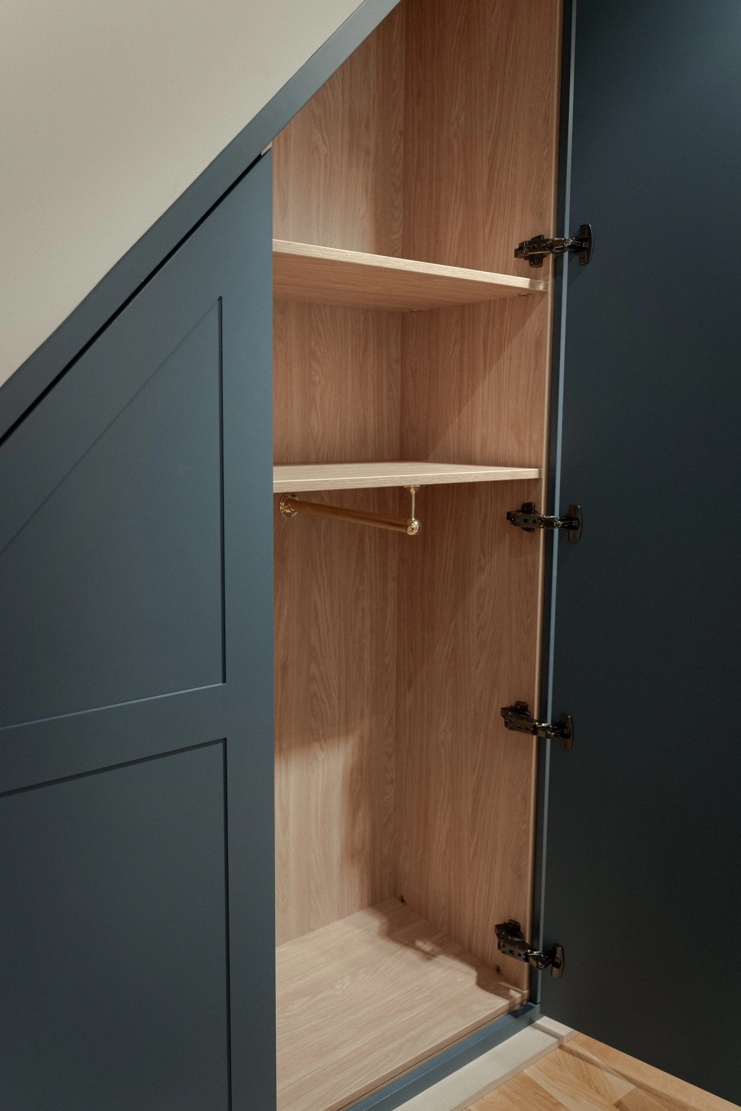 Open blue cabinet with natural wood interior and empty shelves, including a gold-colored hanging rod.