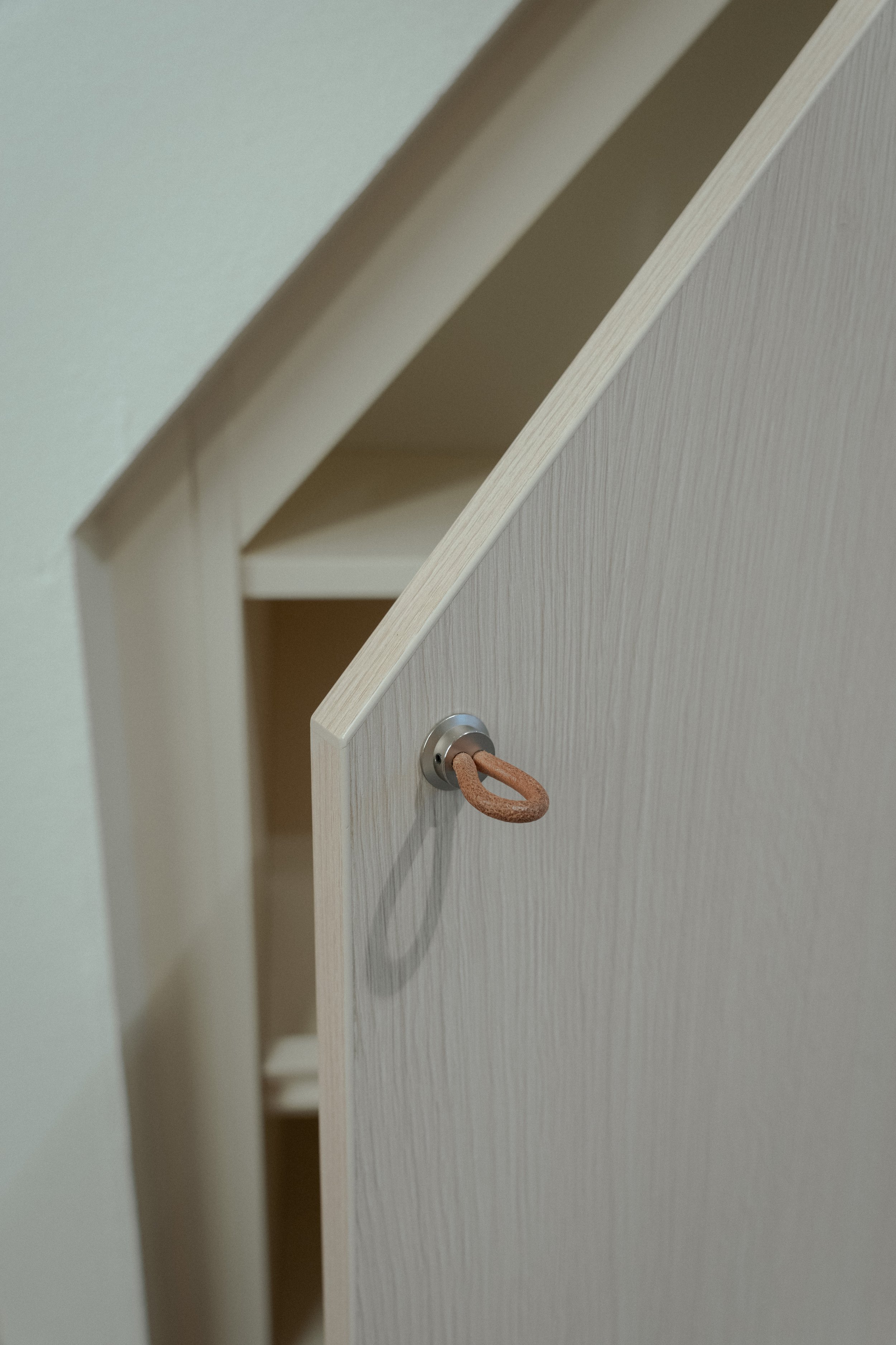 Close-up of a door with a small metal hook with a leather loop, slightly open revealing shelves inside.
