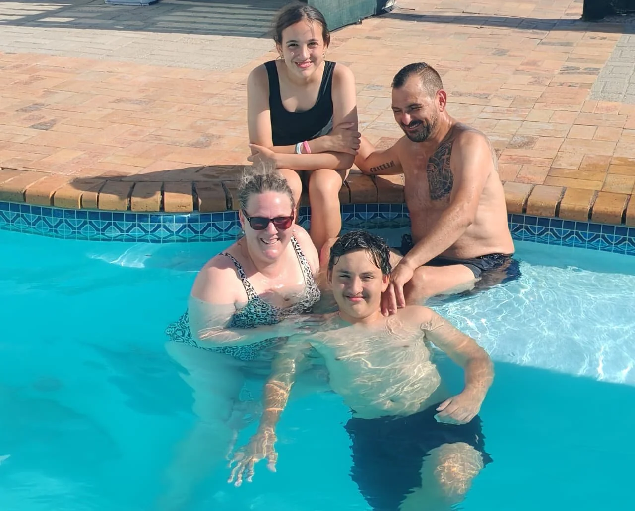 A group of five people enjoying time in a swimming pool, with some sitting on the edge and others in the water, smiling and having fun.
