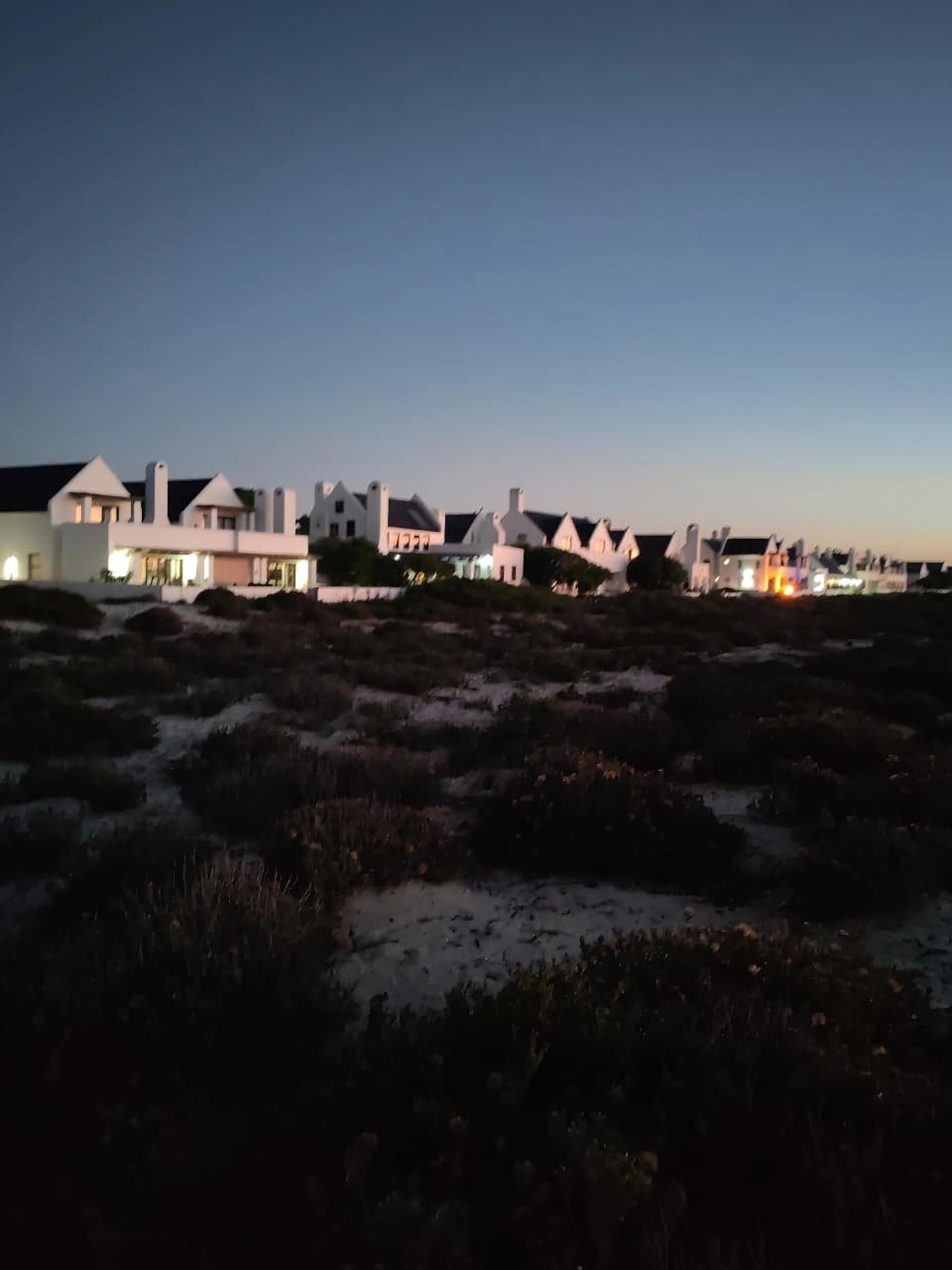 Nighttime view of coastal houses with white exterior walls and pitched roofs, set against a darkening sky.