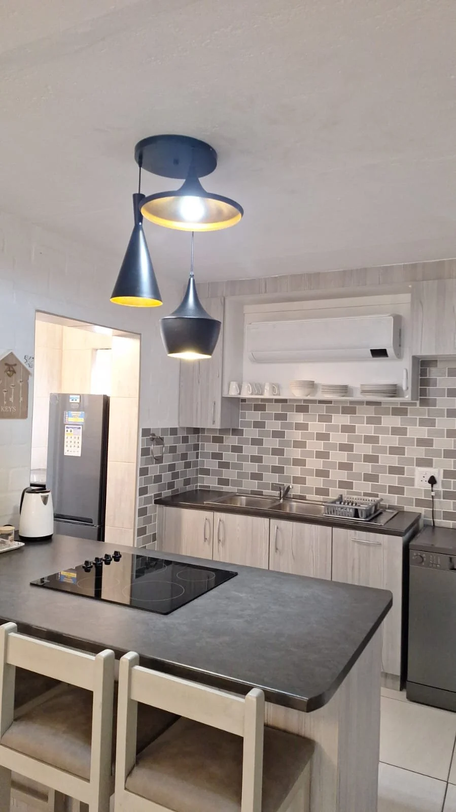 Modern kitchen with pendant lights, brick backsplash, and appliances including refrigerator, stove, dishwasher, and microwave. White cabinets and a countertop with a sink.