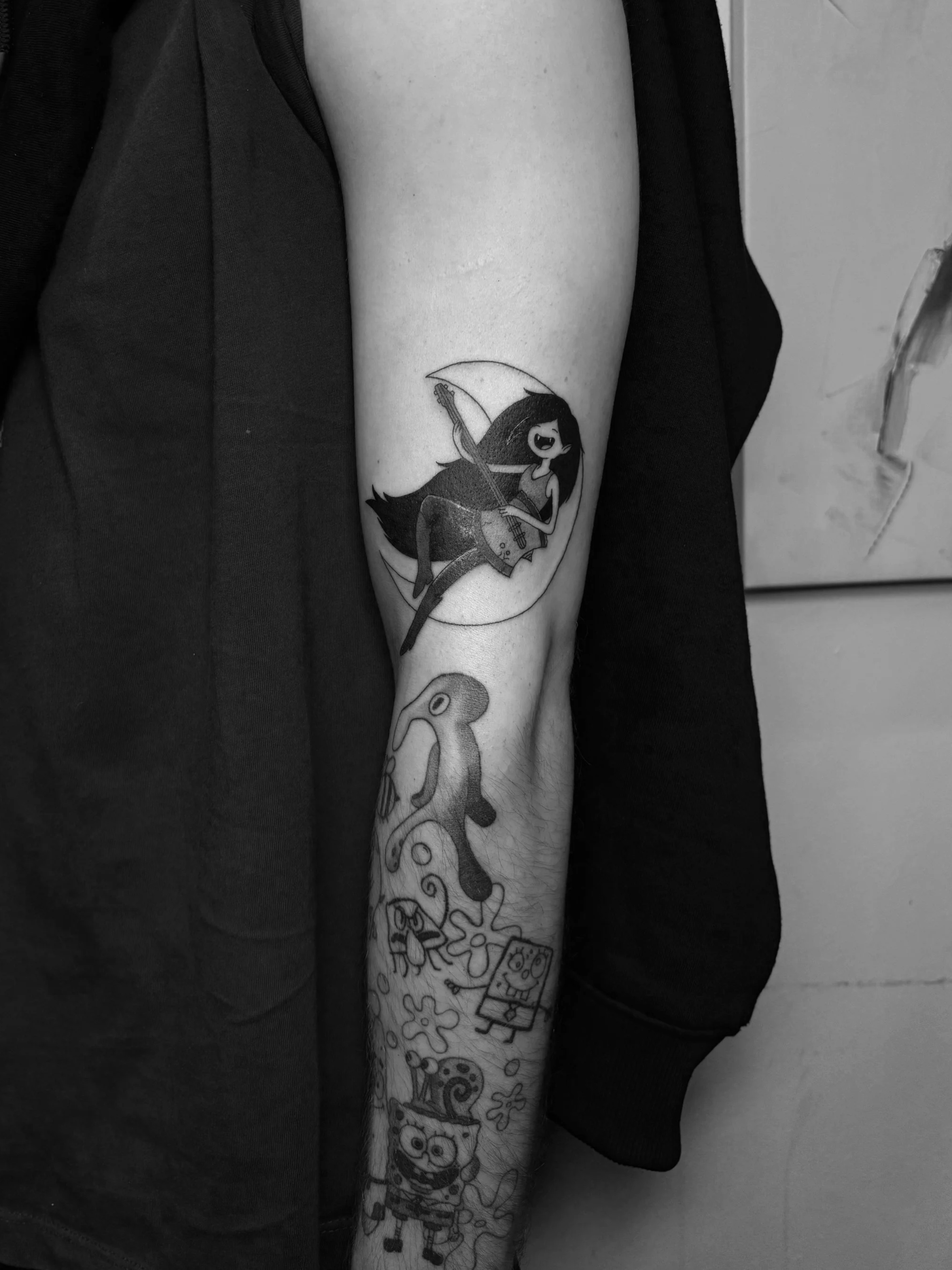 Tattoo eines Mädchens mit E-Gitarre, im Hintergrund Mondsichel, auf dem Unterarm einer Person, in Schwarz-Weiß.