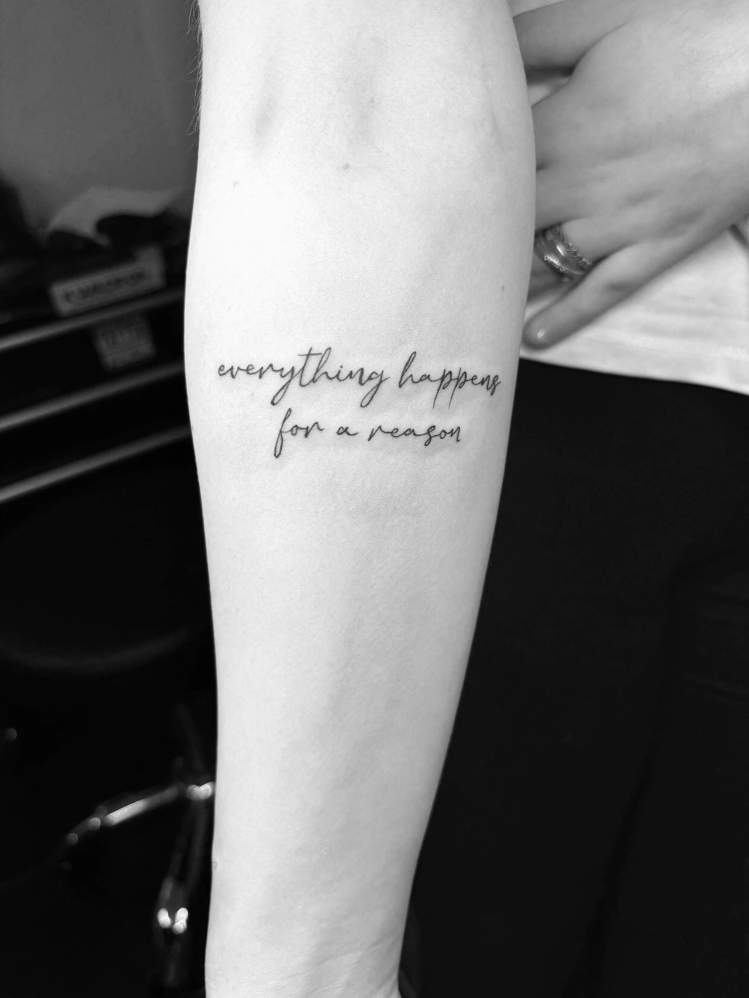 Schwarz-weiße Tätowierung auf einem Arm, der Text lautet 'everything happens for a reason'.