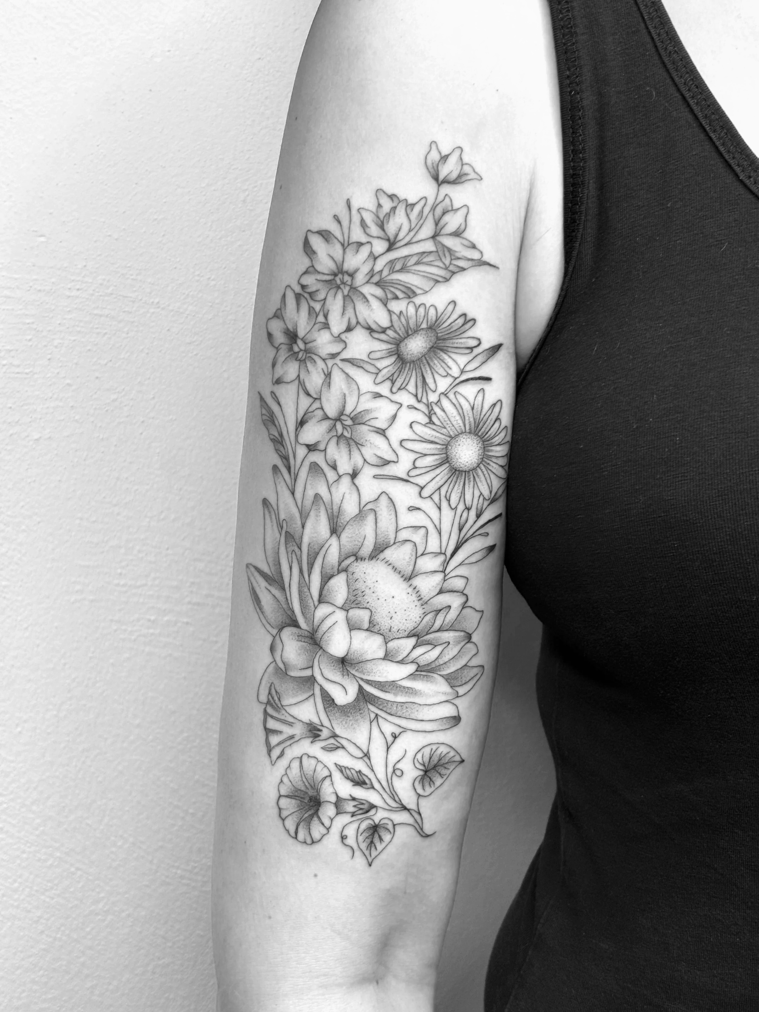 Schwarz-weiß-Tattoo eines Blumenmusters auf dem Oberarm einer Person, die einen schwarzen Oberteil trägt.