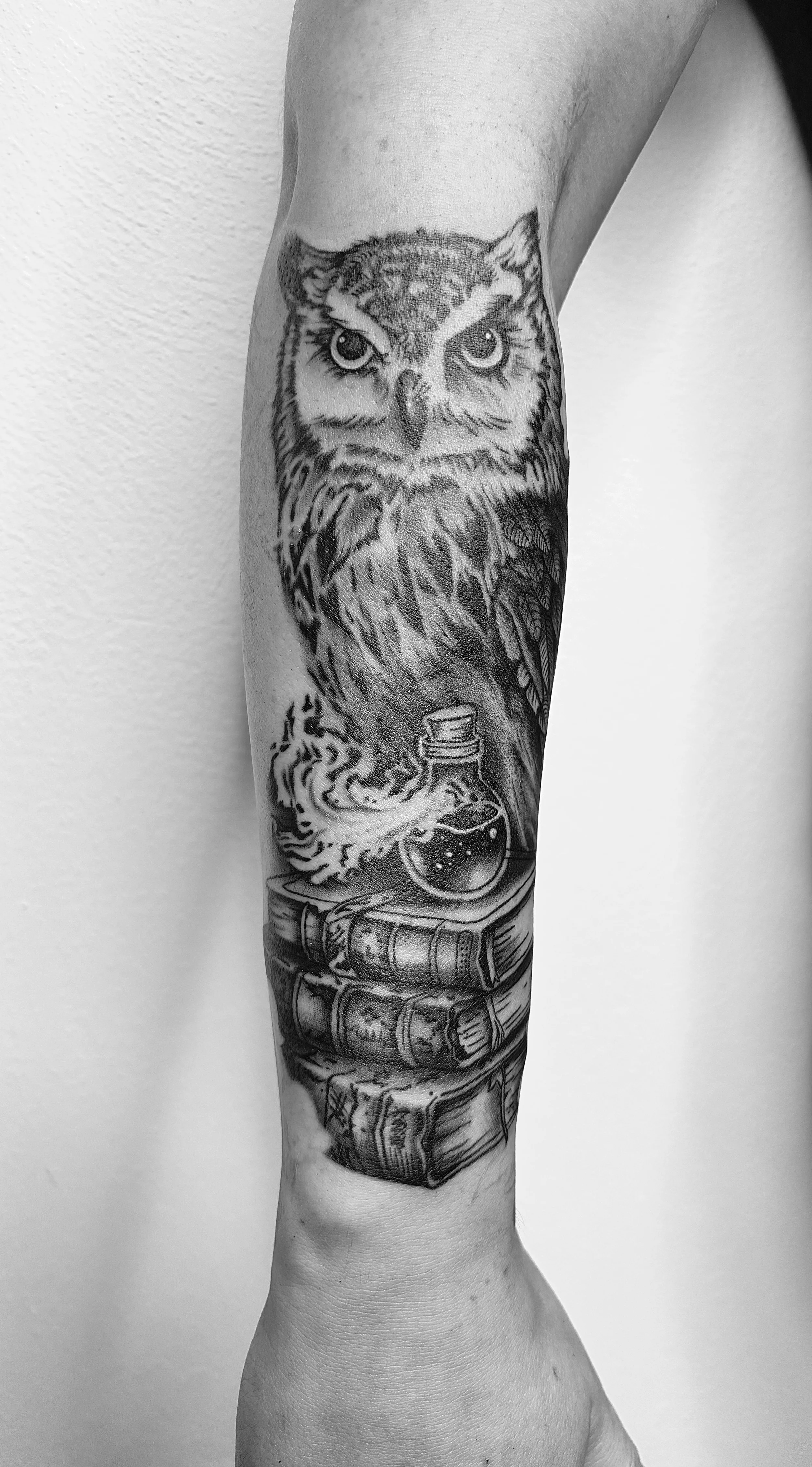 Tattoo eines uhuähnlichen Vogels, der aus einem Zaubertrank brennt, auf dem Arm.