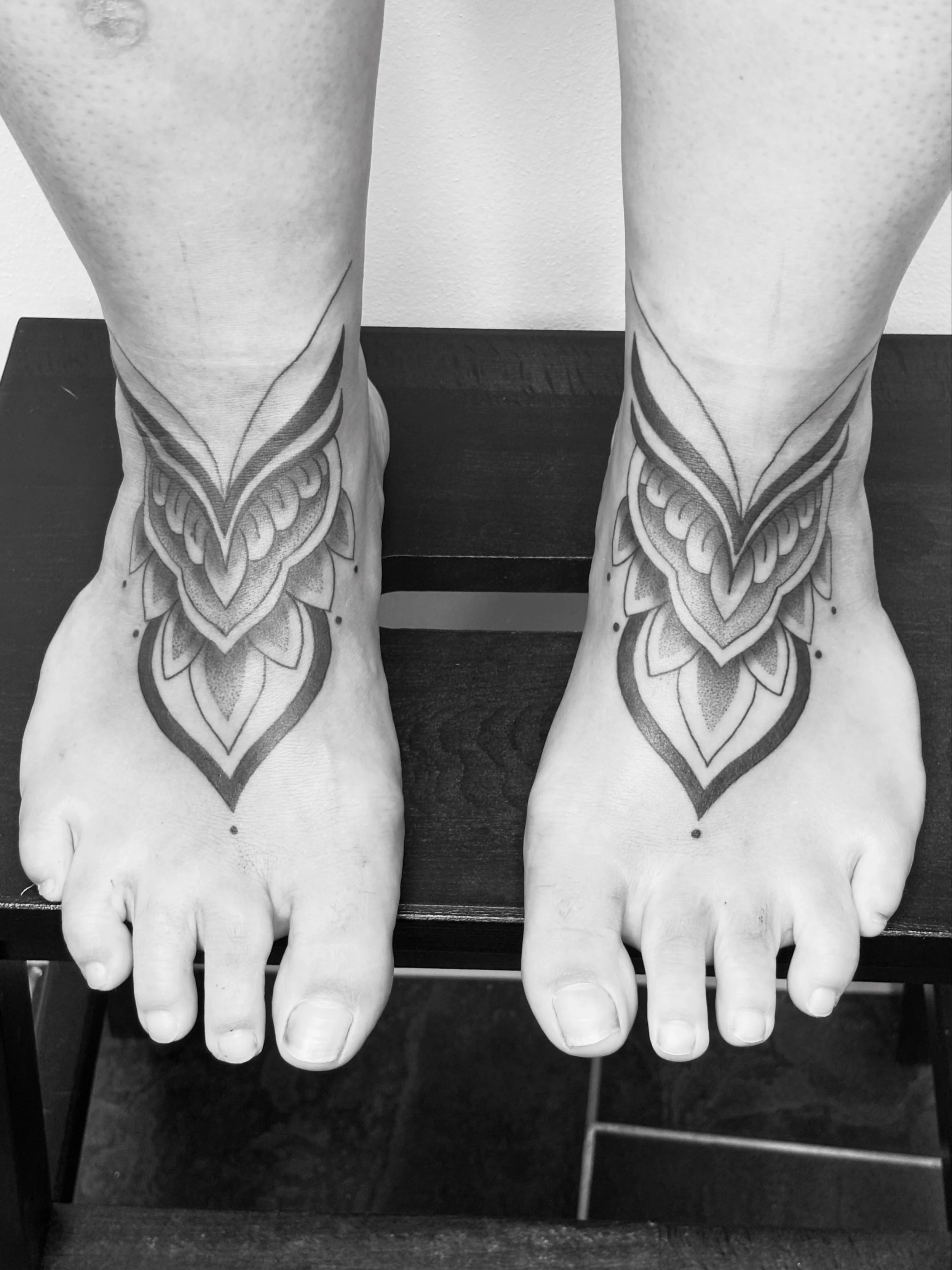 Zwei menschliche Füße mit Tattoo-Designs, die auf einer schwarzen Oberfläche liegen.