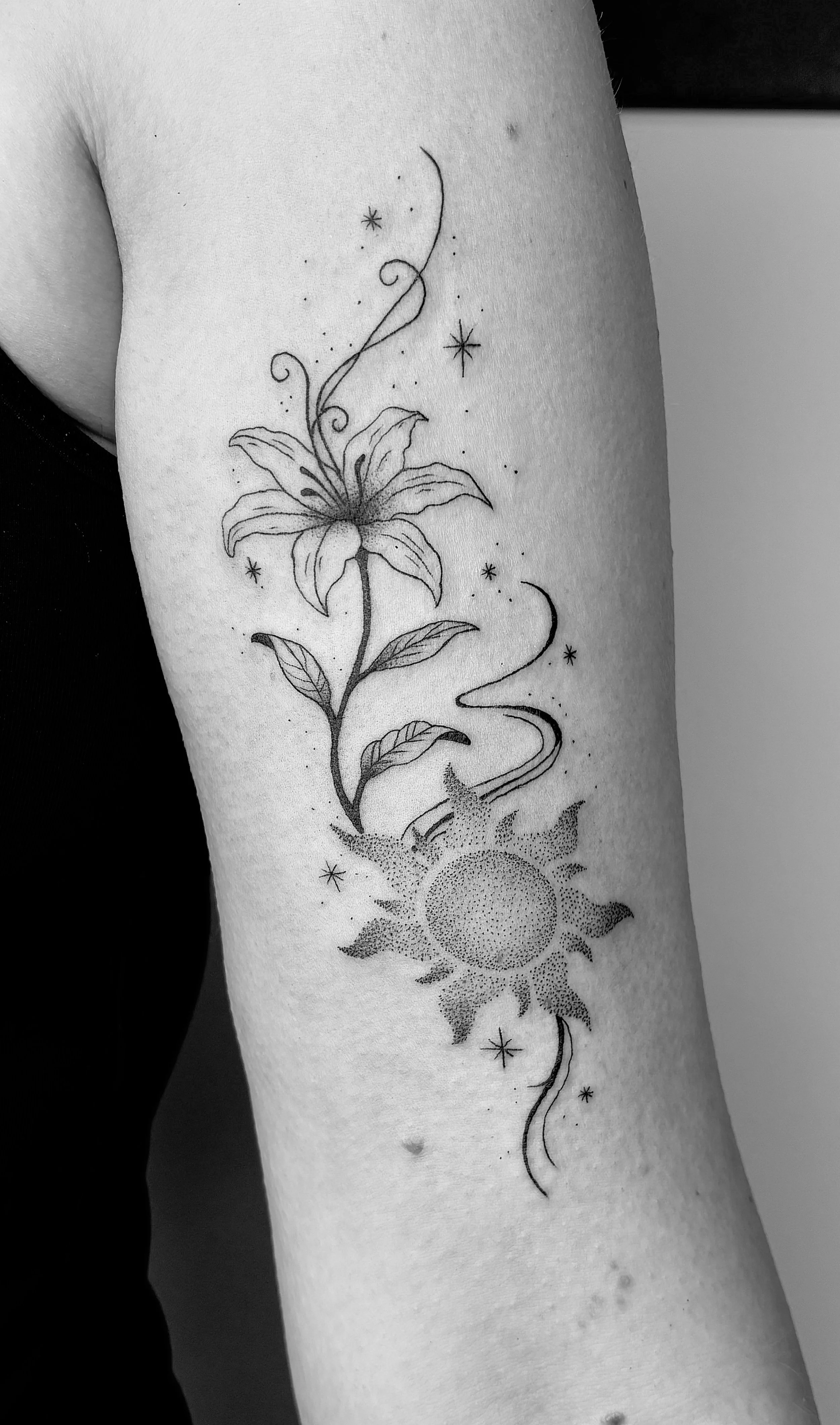 Schwarze Tätowierung eines Lilienblattes, Sternen und einer Sonne auf dem Arm