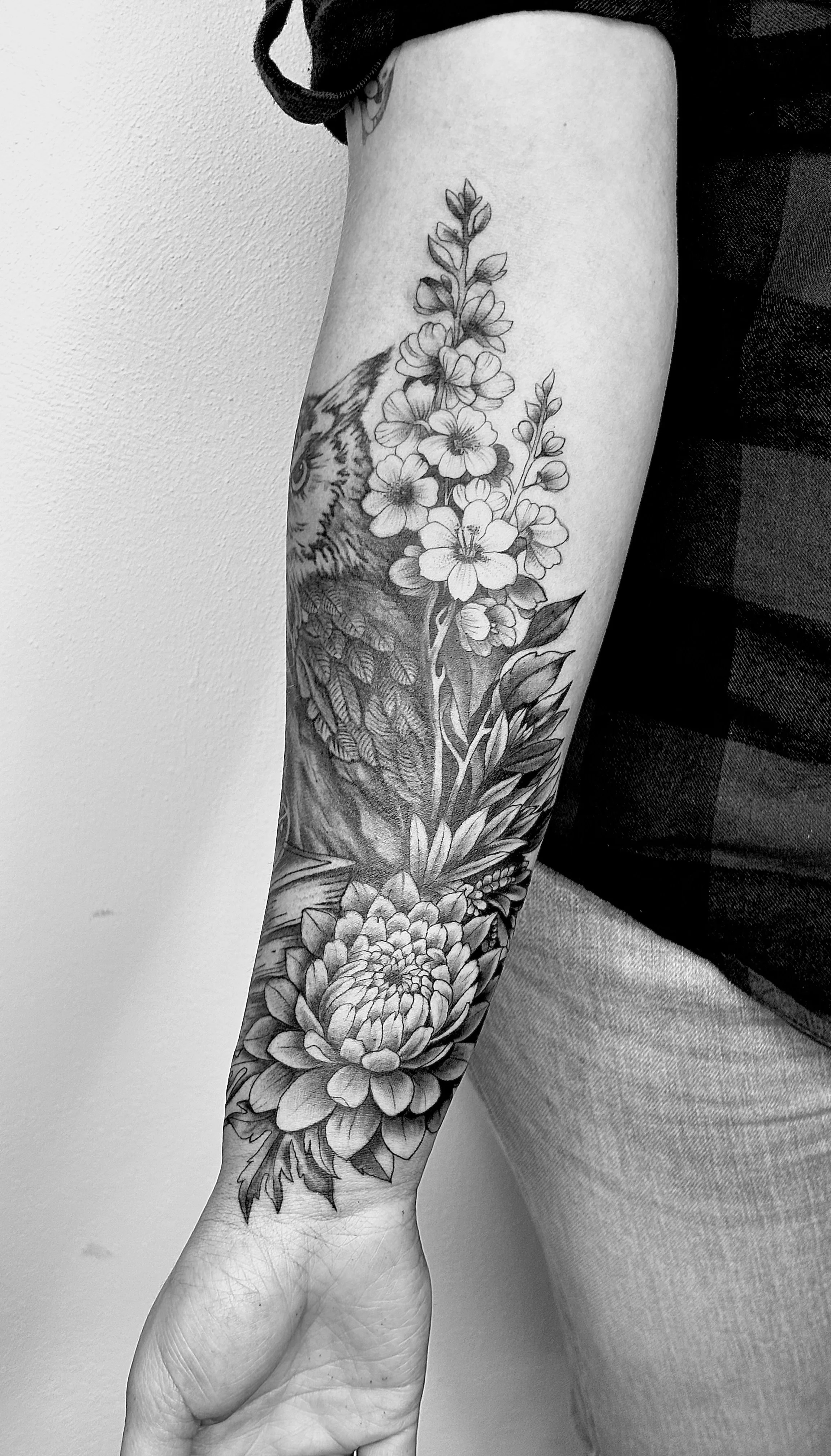 Schwarze Tätowierung eines Blumenstraußes auf einem Arm, detaillierte Linienzeichnung in Schwarz-Weiß.