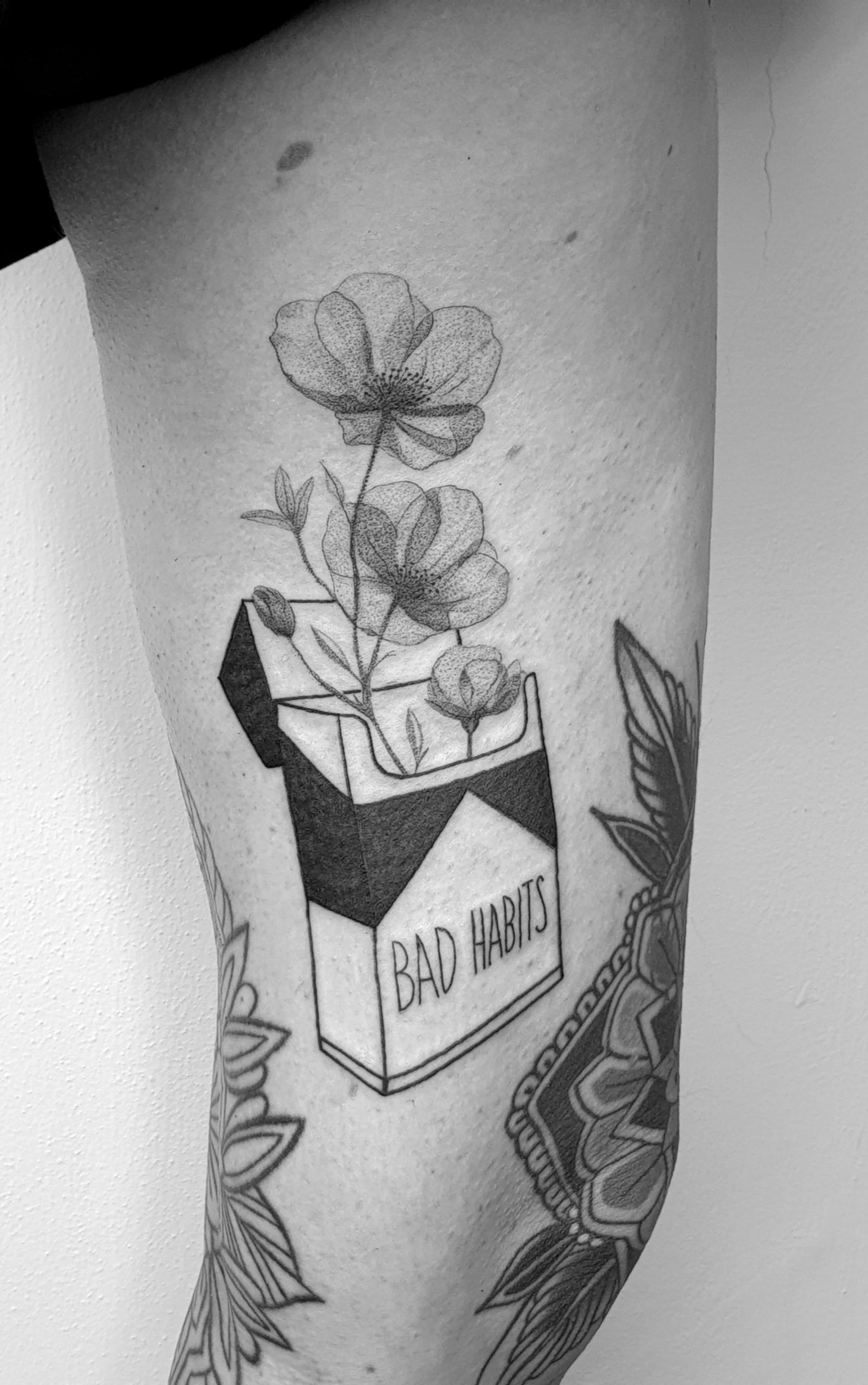 Schwarz-weiß-Tattoo eines Blumenstraußes mit einem Paket, das den Schriftzug "Bad Habits" trägt, auf einem Arm.