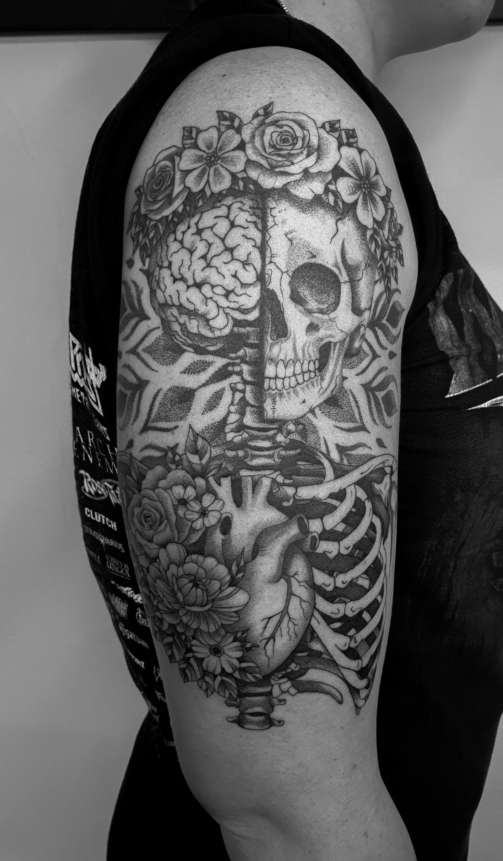 Schultertattoo eines menschlichen Schädels mit Blumen und einem Gehirn, in schwarz-weiß.