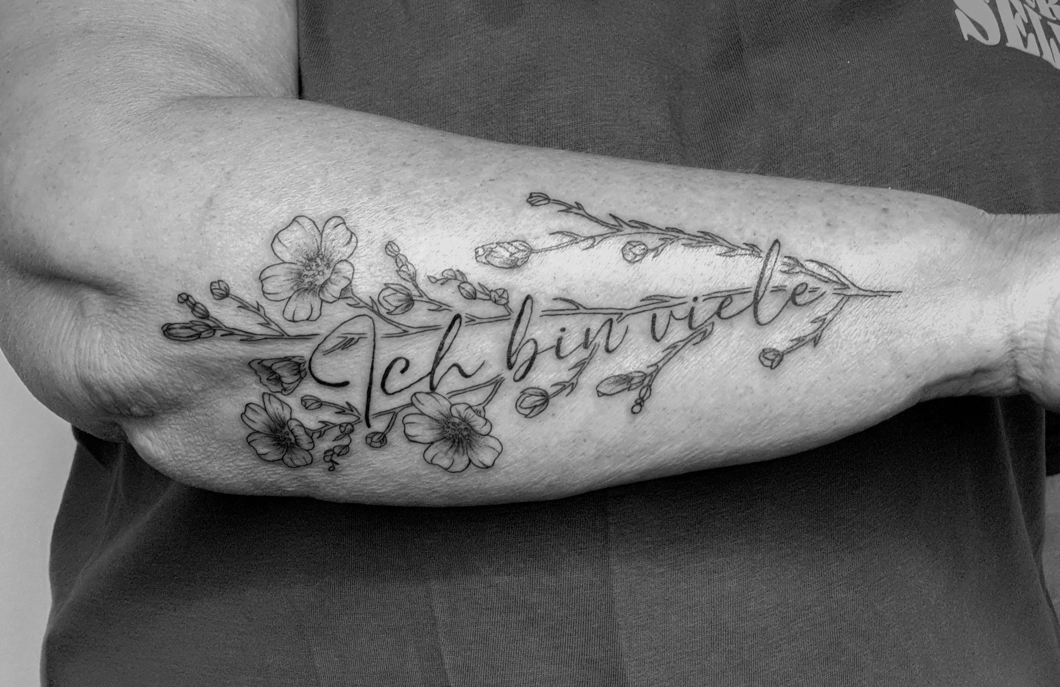 Schwarze Tätowierung eines Blumenmusters auf dem Unterarm, inklusive Text 'Ich liebe dich'.
