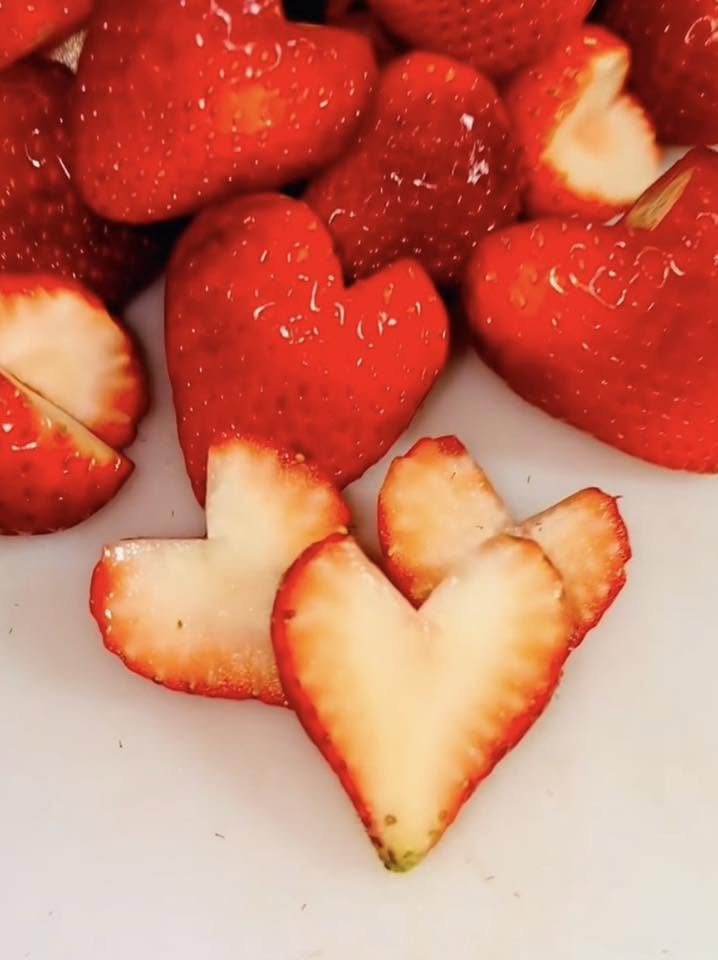 Close-up of fresh strawberries, some sliced and some whole, on a white surface.