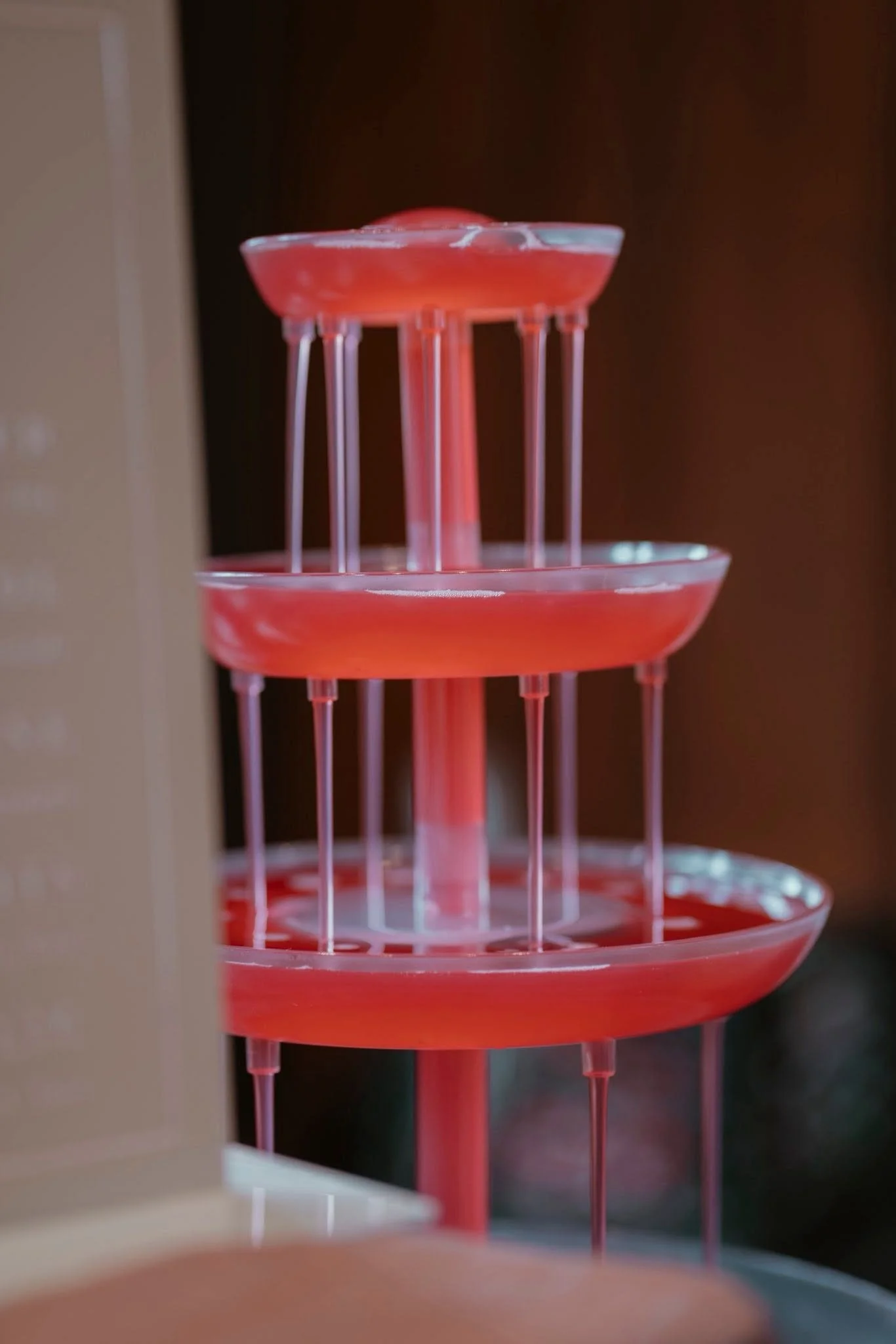 Close-up of a pink and clear multi-tiered plastic stand or organizer, possibly holding jewelry or small items, with a blurred background.
