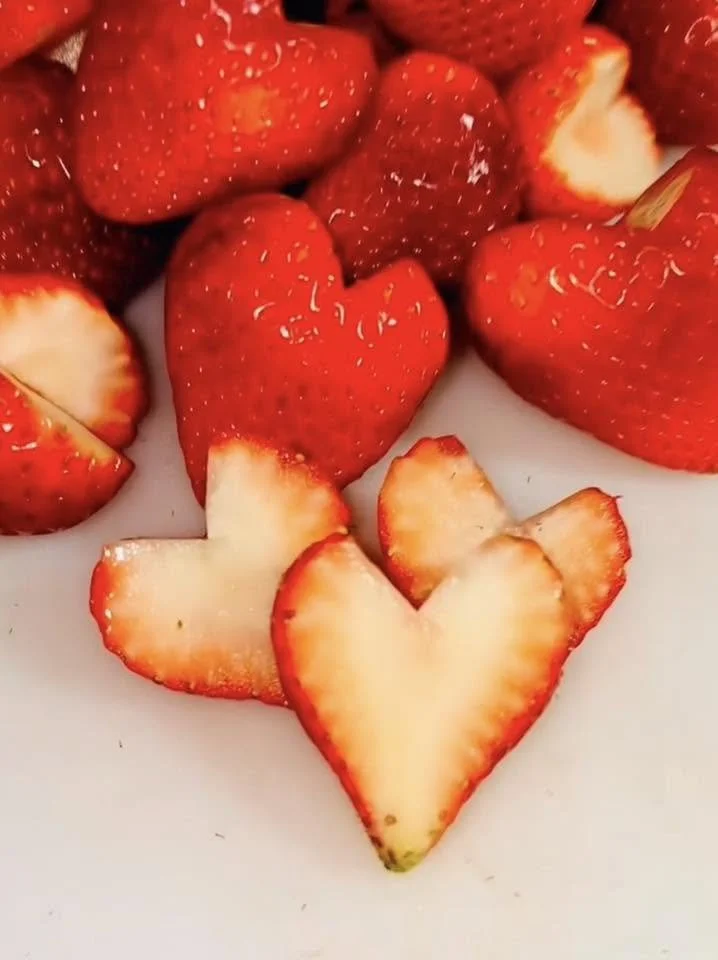 Fresh strawberries, some sliced and some whole, on a white surface.