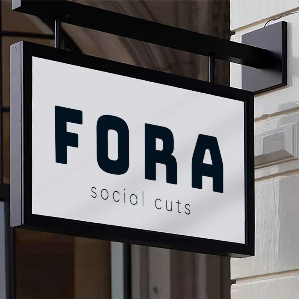 Sign for a salon called 'FORA Social Cuts' with black frame, mounted on the wall outside.