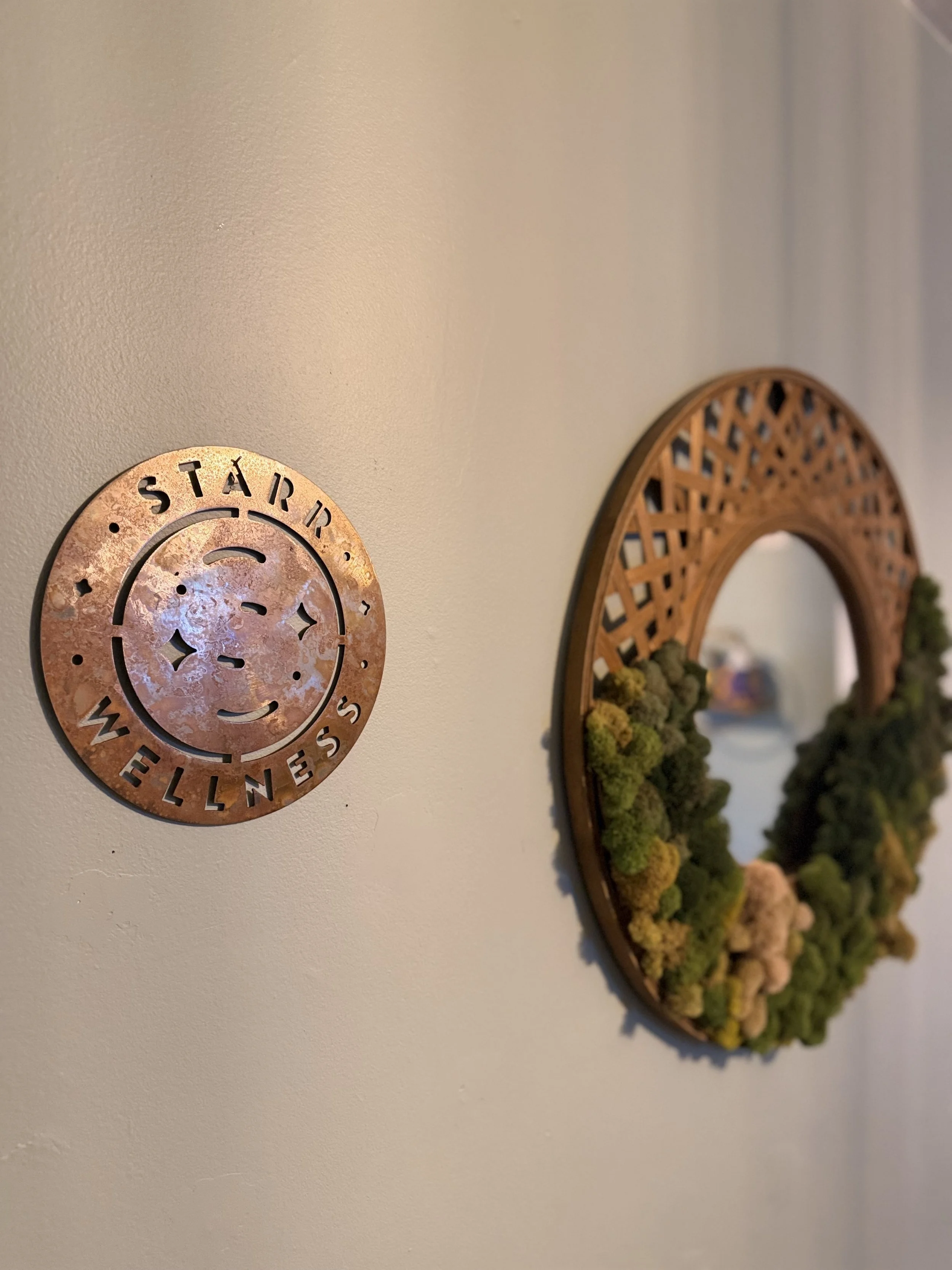 Copper star-themed wall plaque beside an ornate arched mirror with greenery
