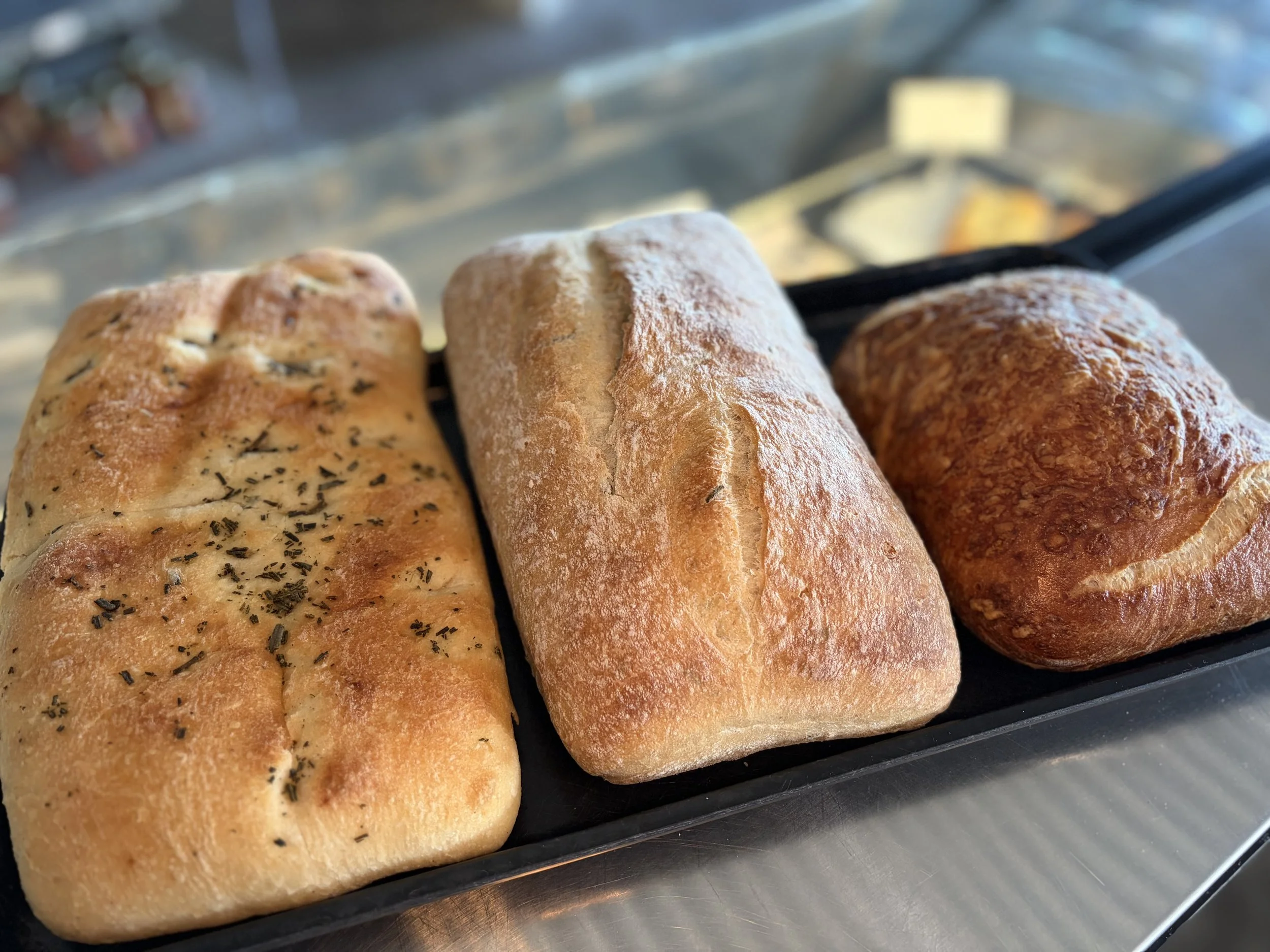 Three freshly baked loaves of bread, each with different toppings, resting on a black baking tray.
