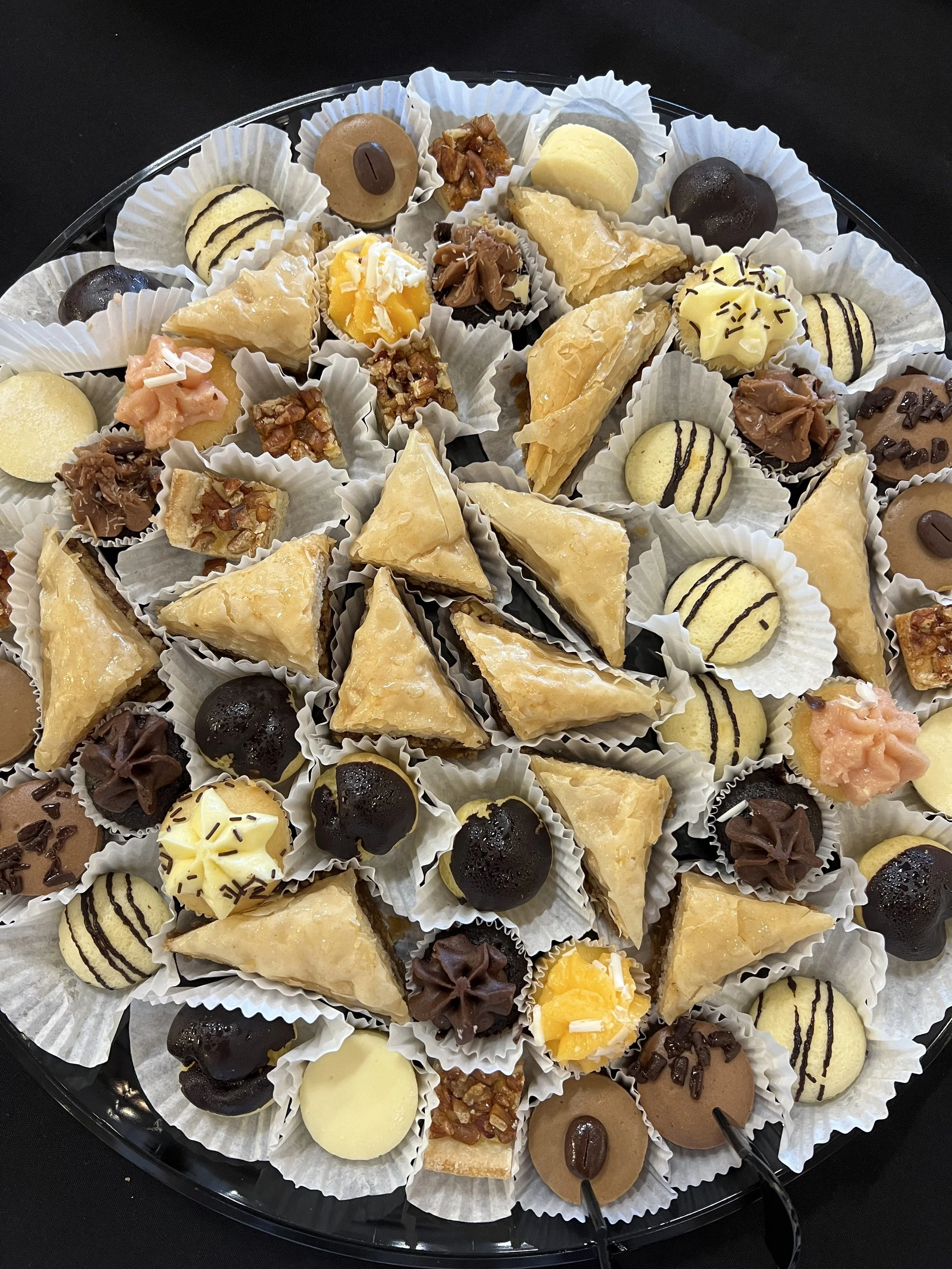 A tray of assorted mini desserts, including cookies, cream puffs, pastries, and candies, all arranged in paper cups.
