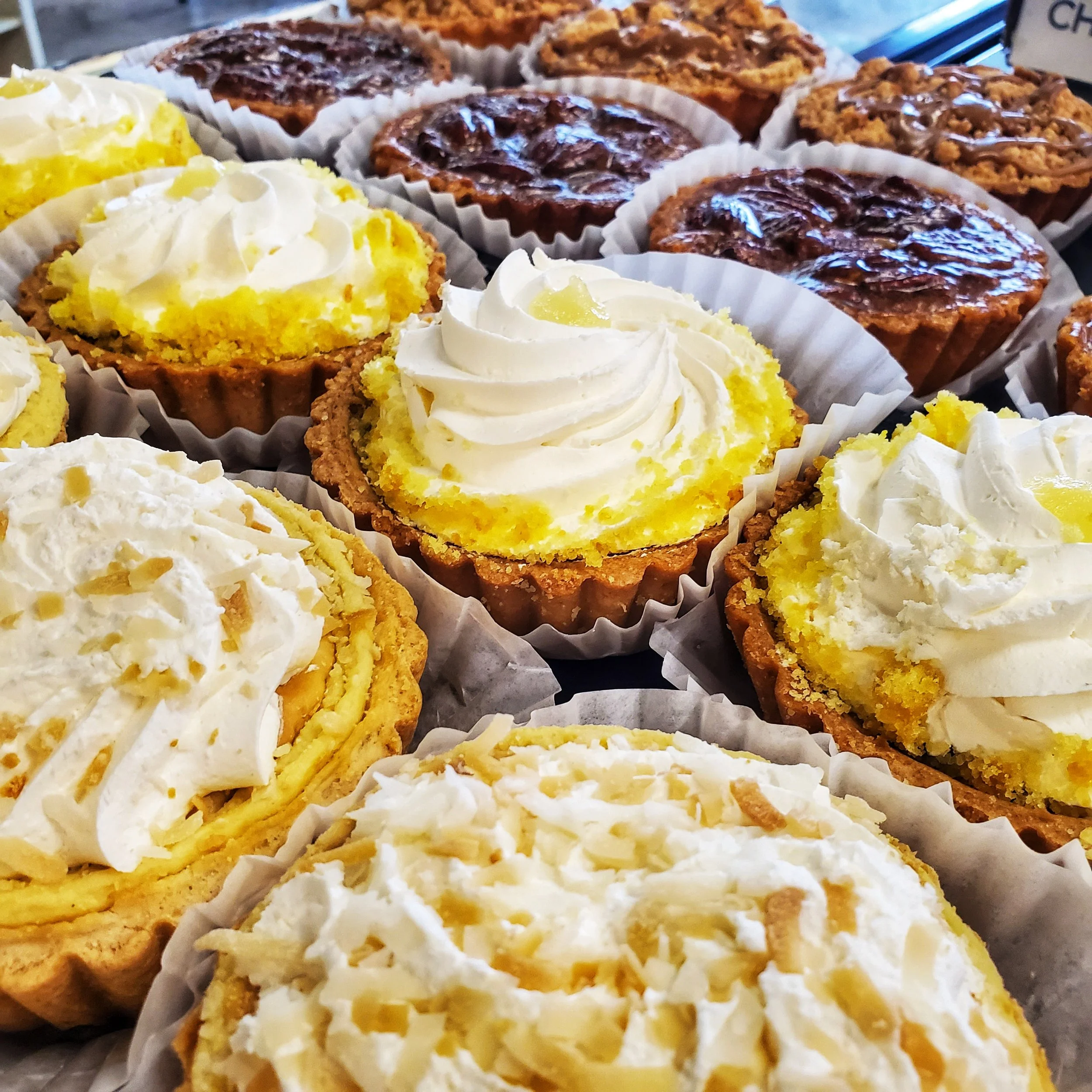 Close-up of various cupcakes, some topped with white frosting and yellow sprinkles, others with chocolate or nut toppings.