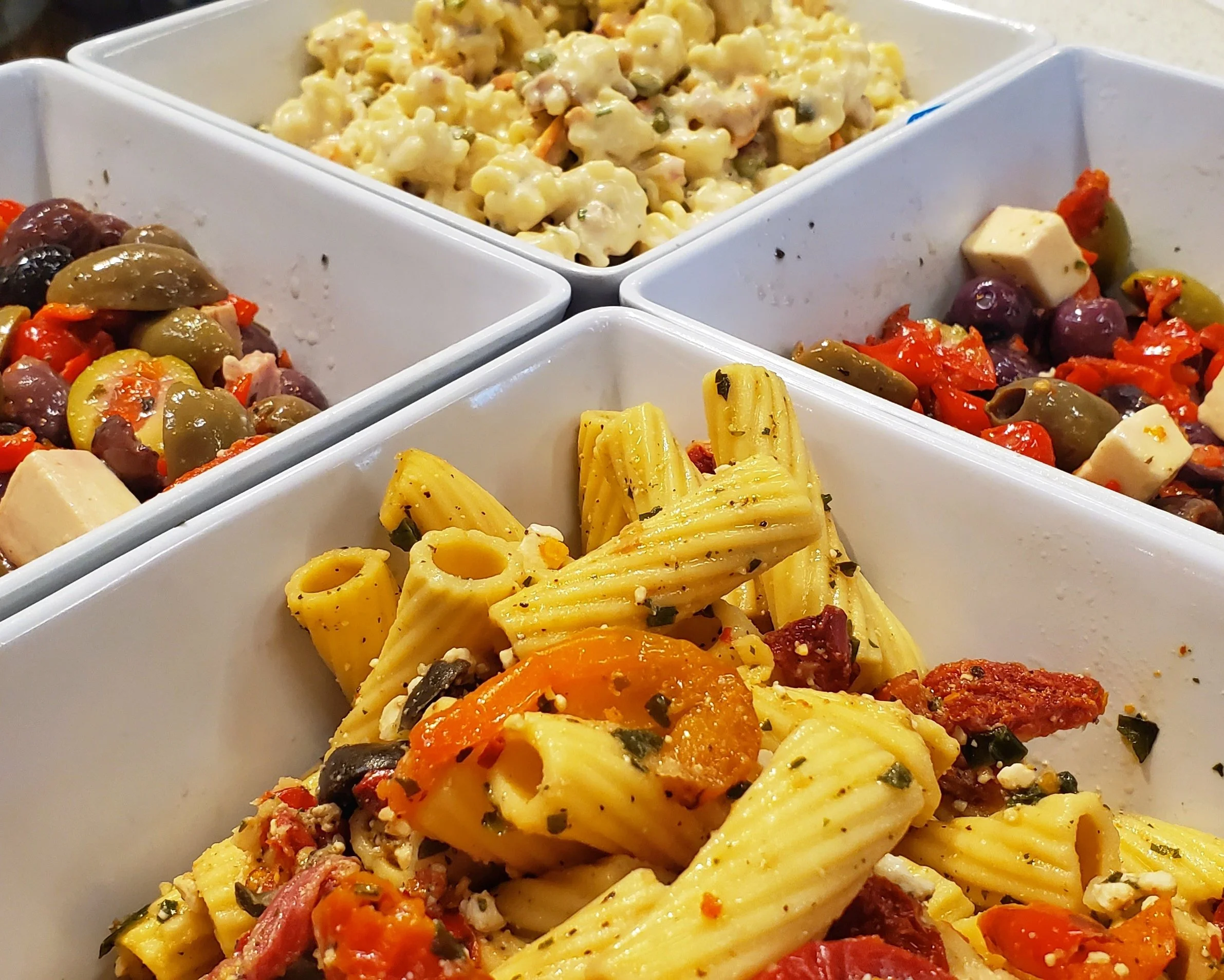 Close-up of three white sections filled with pasta salad, marinated olives, and cheese cubes with vegetables.
